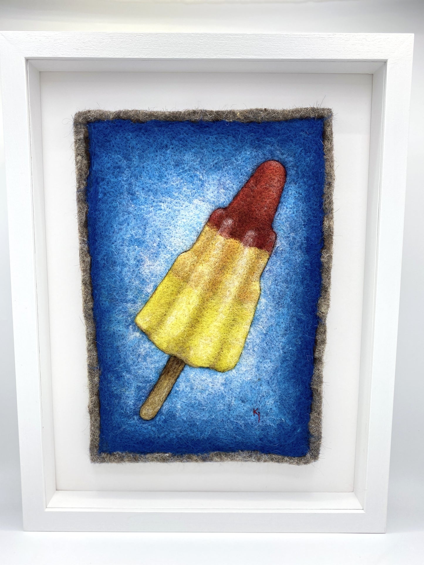 a needle felted picture of a striped red, orange and yellow Rocket ice lolly on a bright blue background