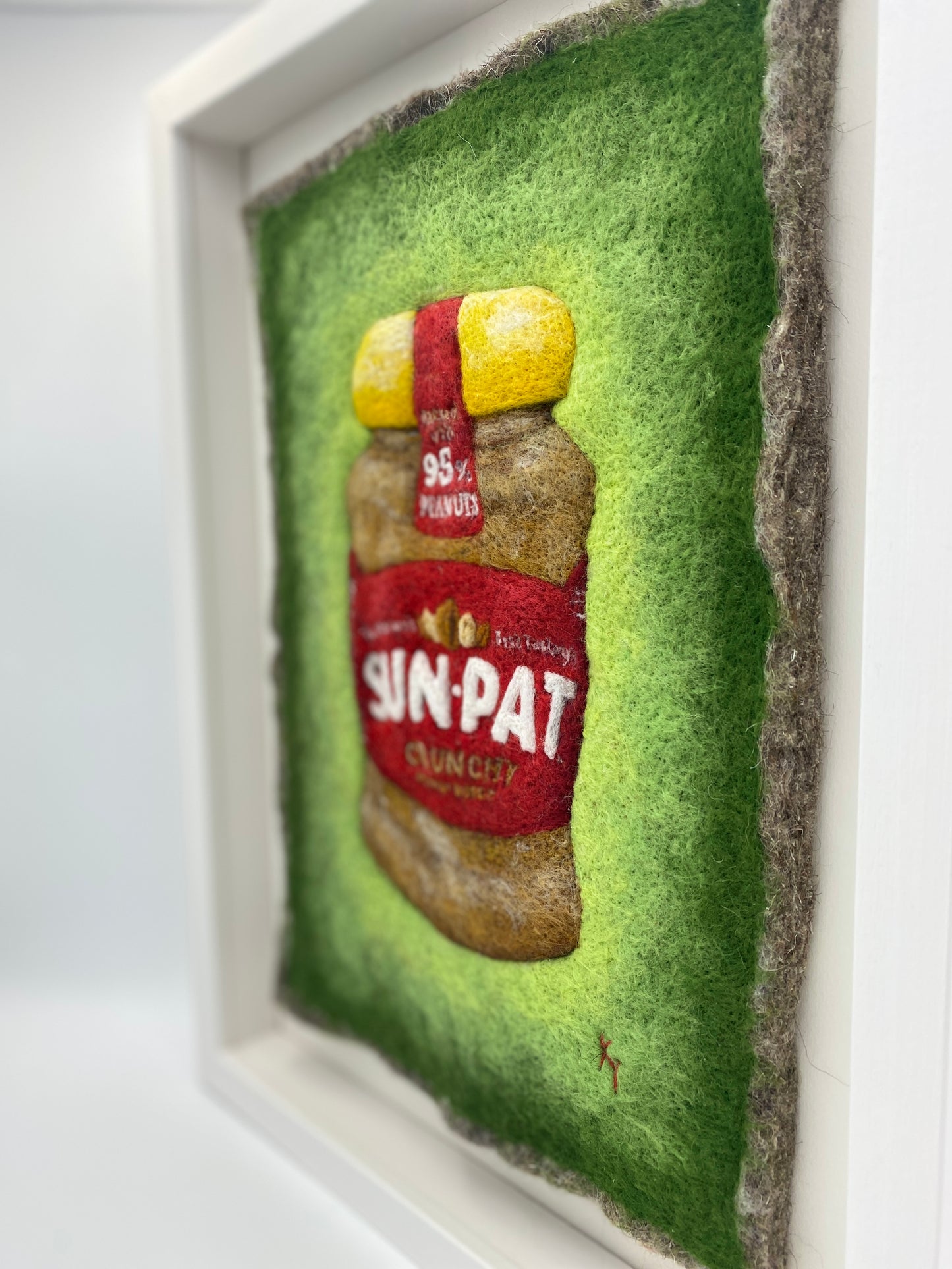 needle felted study of a jar of Sun-Pat peanut butter on a bright green background and framed in a white wooden box frame