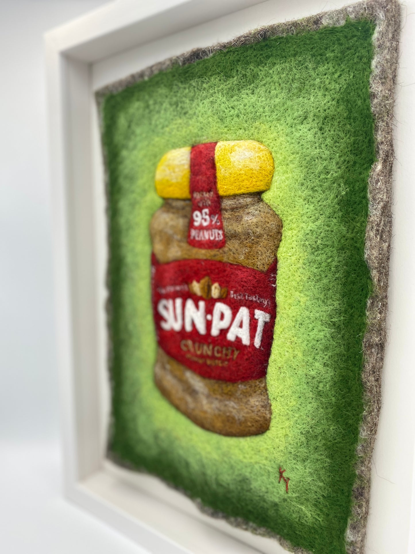 needle felted study of a jar of Sun-Pat peanut butter on a bright green background and framed in a white wooden box frame