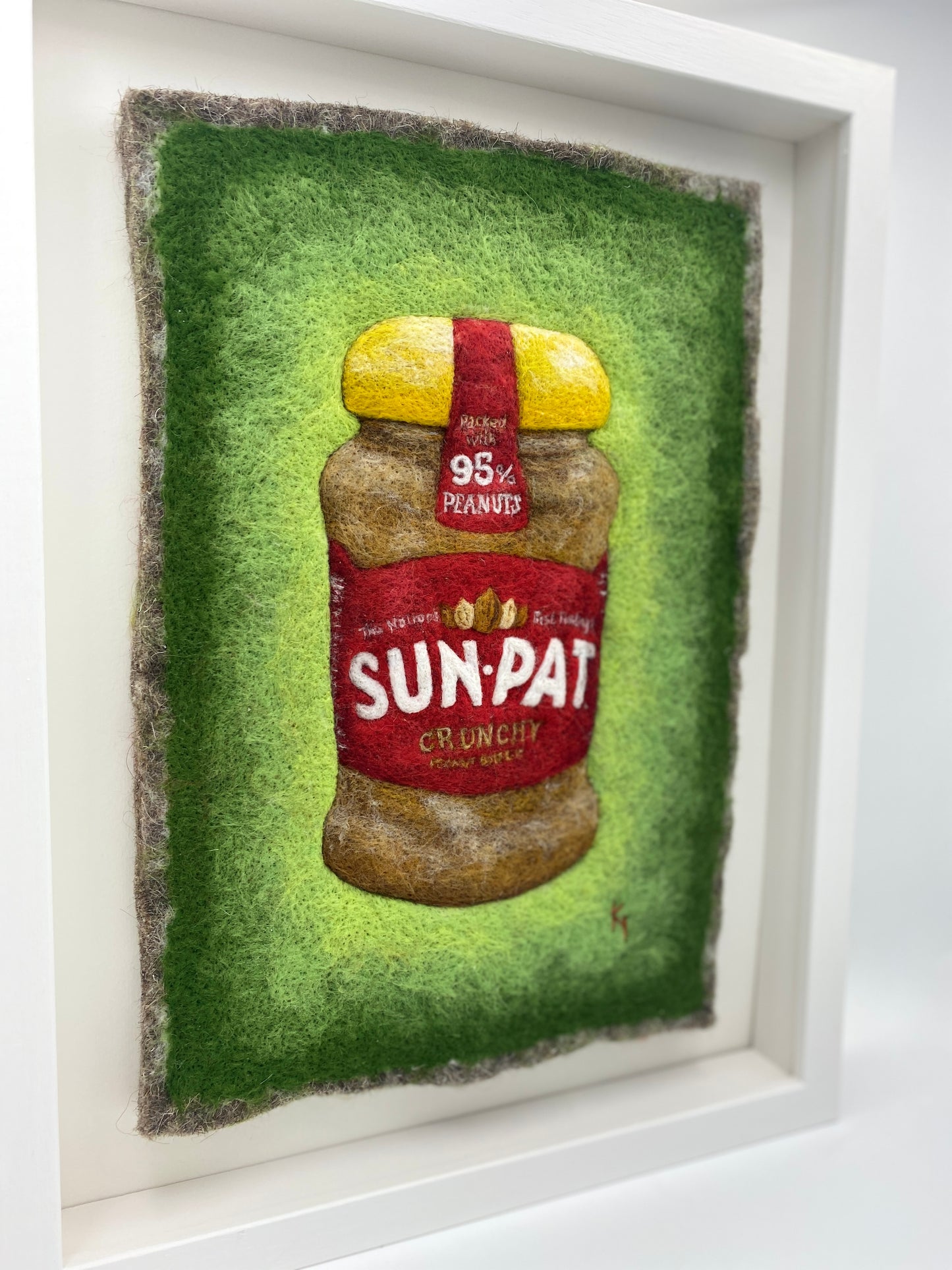 needle felted study of a jar of Sun-Pat peanut butter on a bright green background and framed in a white wooden box frame