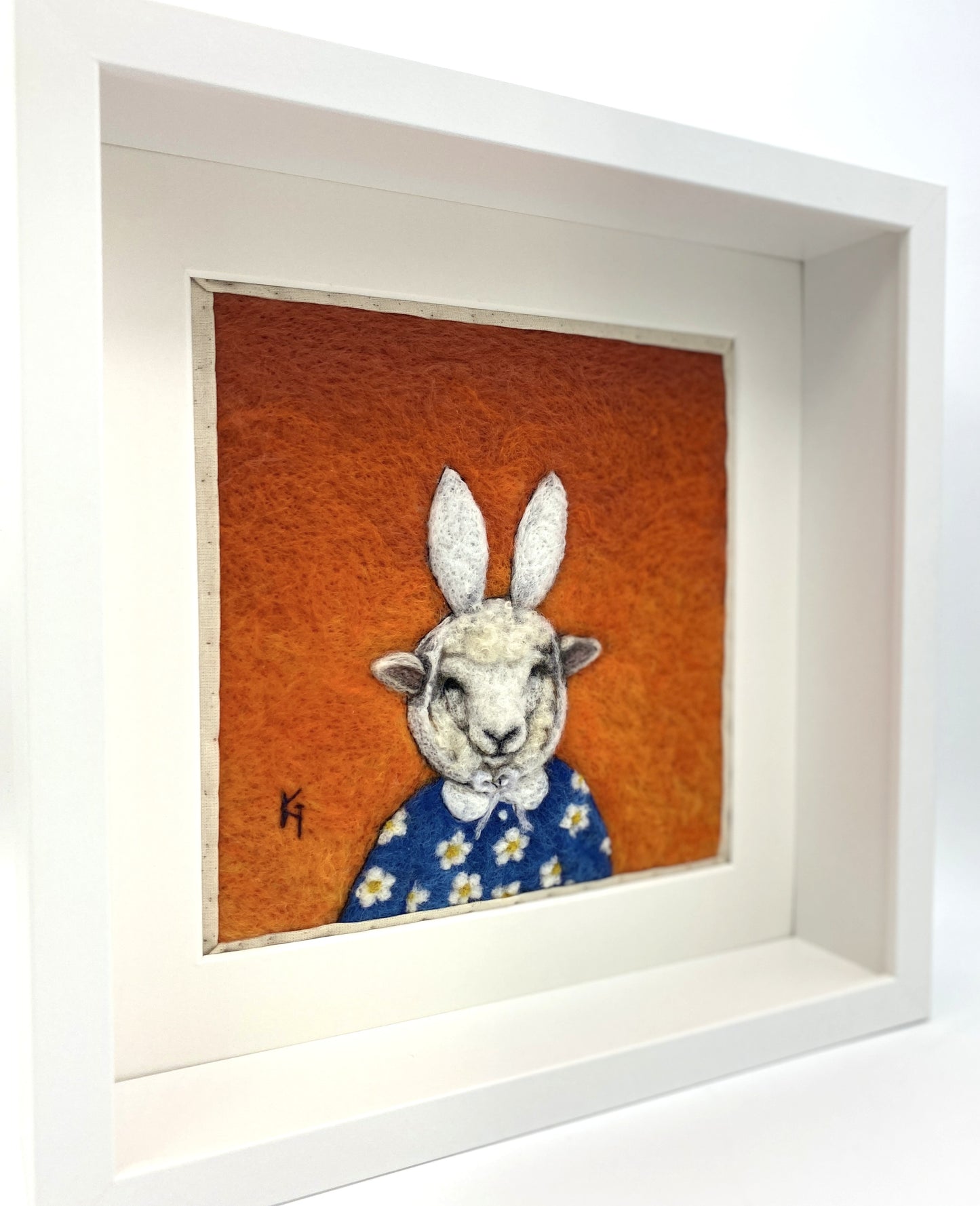 Needle felted picture of a sheep dressed as Miffy in her birthday dress, with an orange background