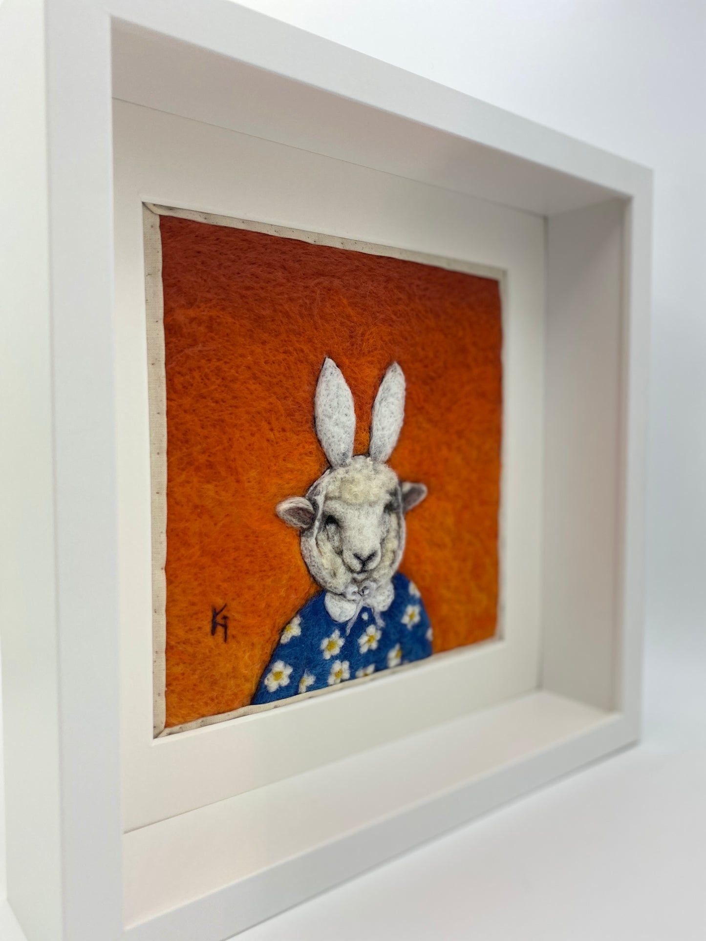Needle felted picture of a sheep dressed as Miffy in her birthday dress, with an orange background