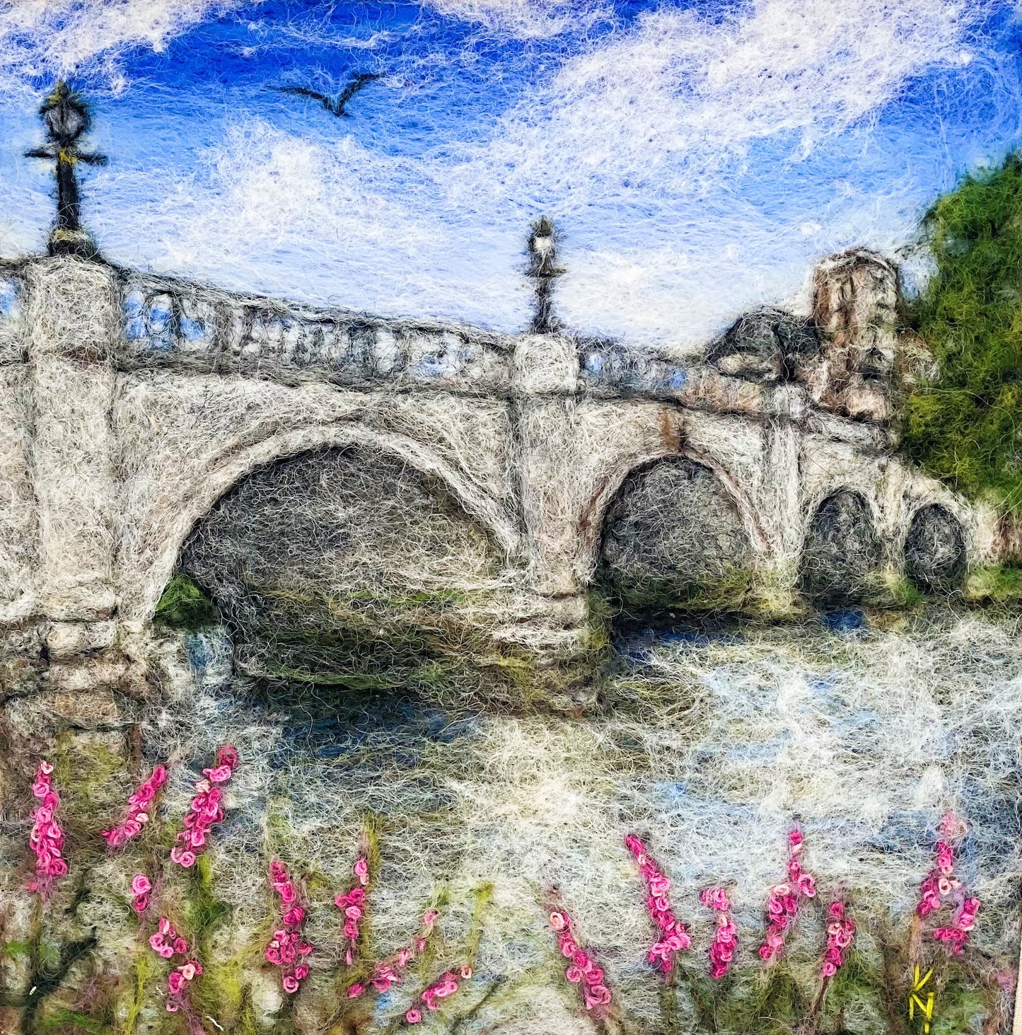 a box-framed, needle felted wool fibre picture of Ricmond Bridge showing the bridge, buildings across the river, trees, lamp posts and embroidered purple wild flowers