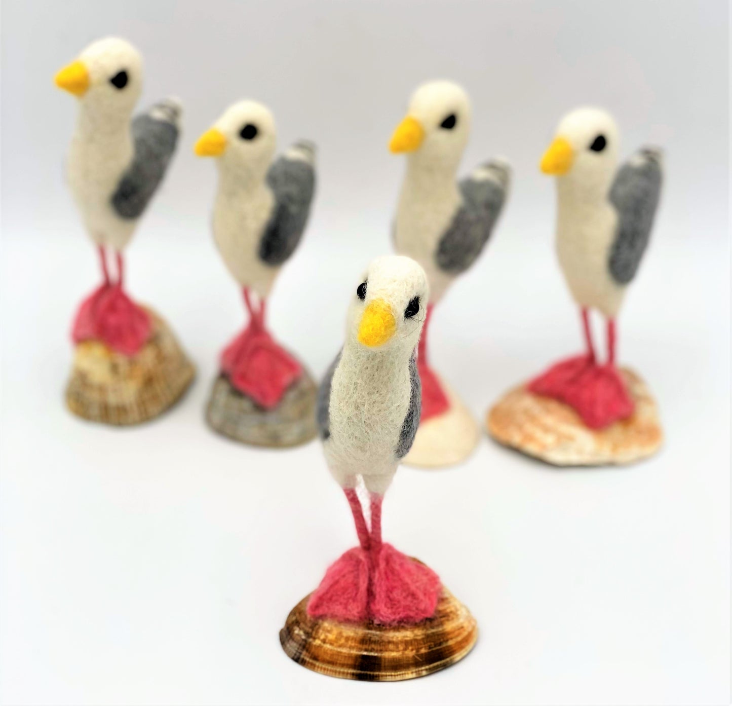 group of five needle felted seagulls standing on sea shells, white, black, grey wings, pink legs and feet