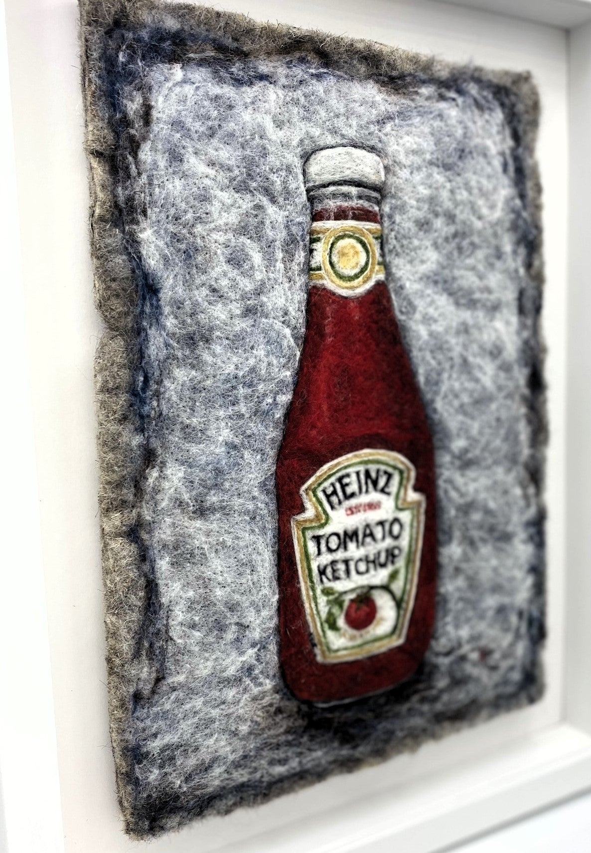 Needle felted study of a glass bottle of Heinz Tomato Ketchup, on blue-grey felted back ground, framed inside a white wooden, glass-fronted box frame white