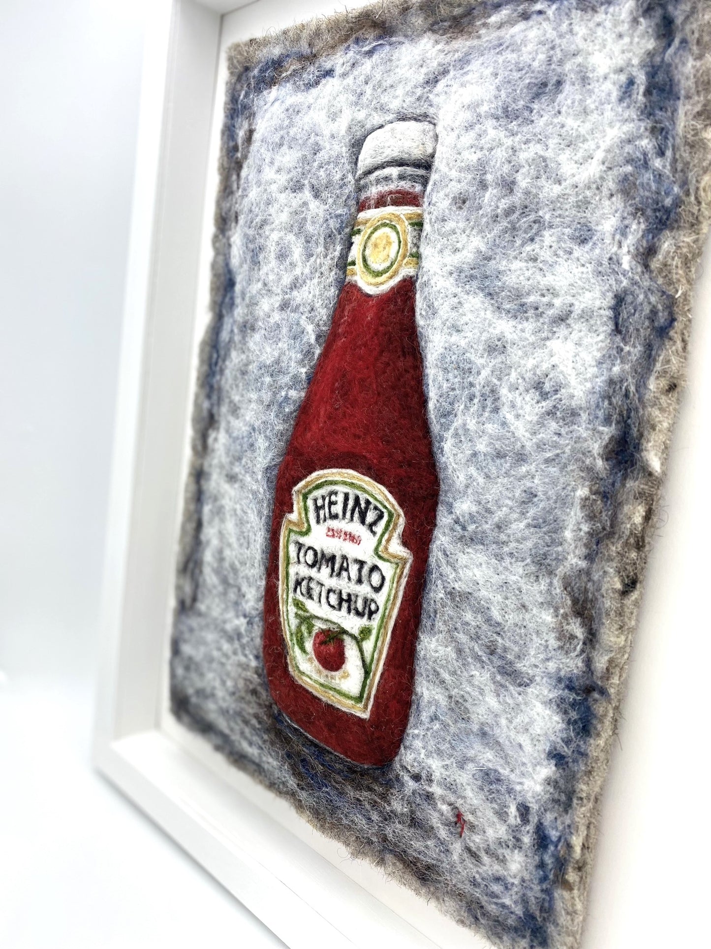 Needle felted study of a glass bottle of Heinz Tomato Ketchup, on blue-grey felted back ground, framed inside a white wooden, glass-fronted box frame white