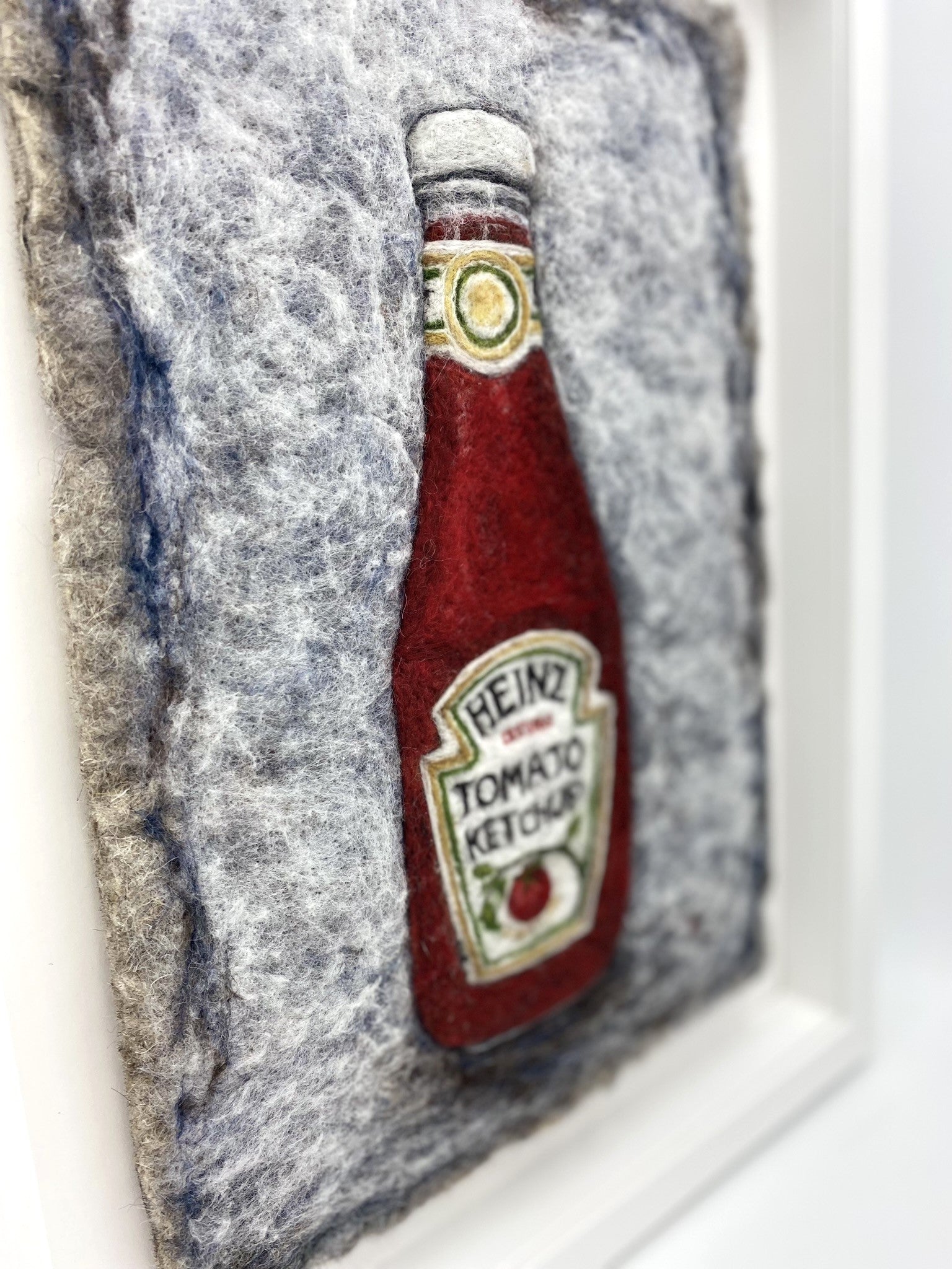 Needle felted study of a glass bottle of Heinz Tomato Ketchup, on blue-grey felted back ground, framed inside a white wooden, glass-fronted box frame white