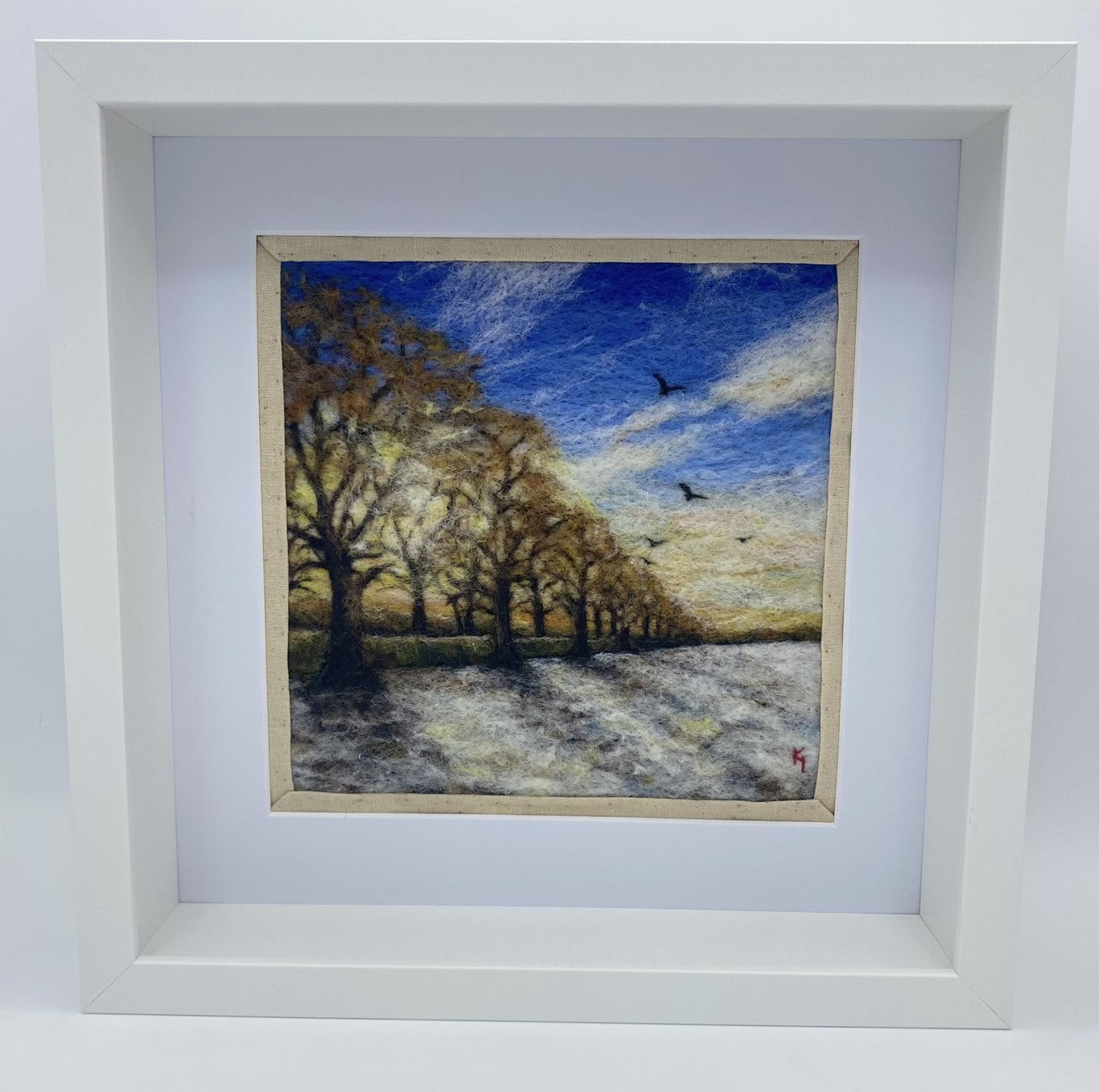 needle felted scene of a wintery sunrise with a row of almost bare trees following a lane to a distant horizon; the trees are casting shadows on a snowy field