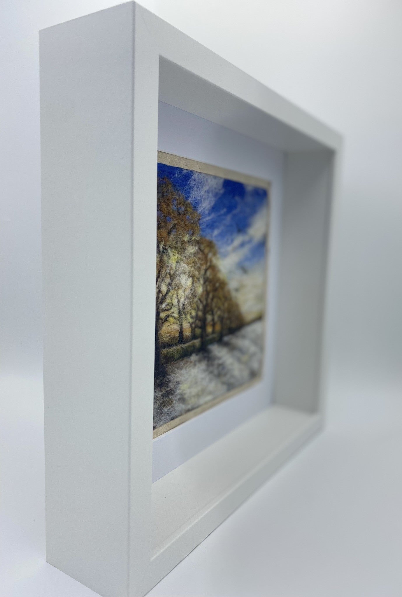 needle felted scene of a wintery sunrise with a row of almost bare trees following a lane to a distant horizon; the trees are casting shadows on a snowy field