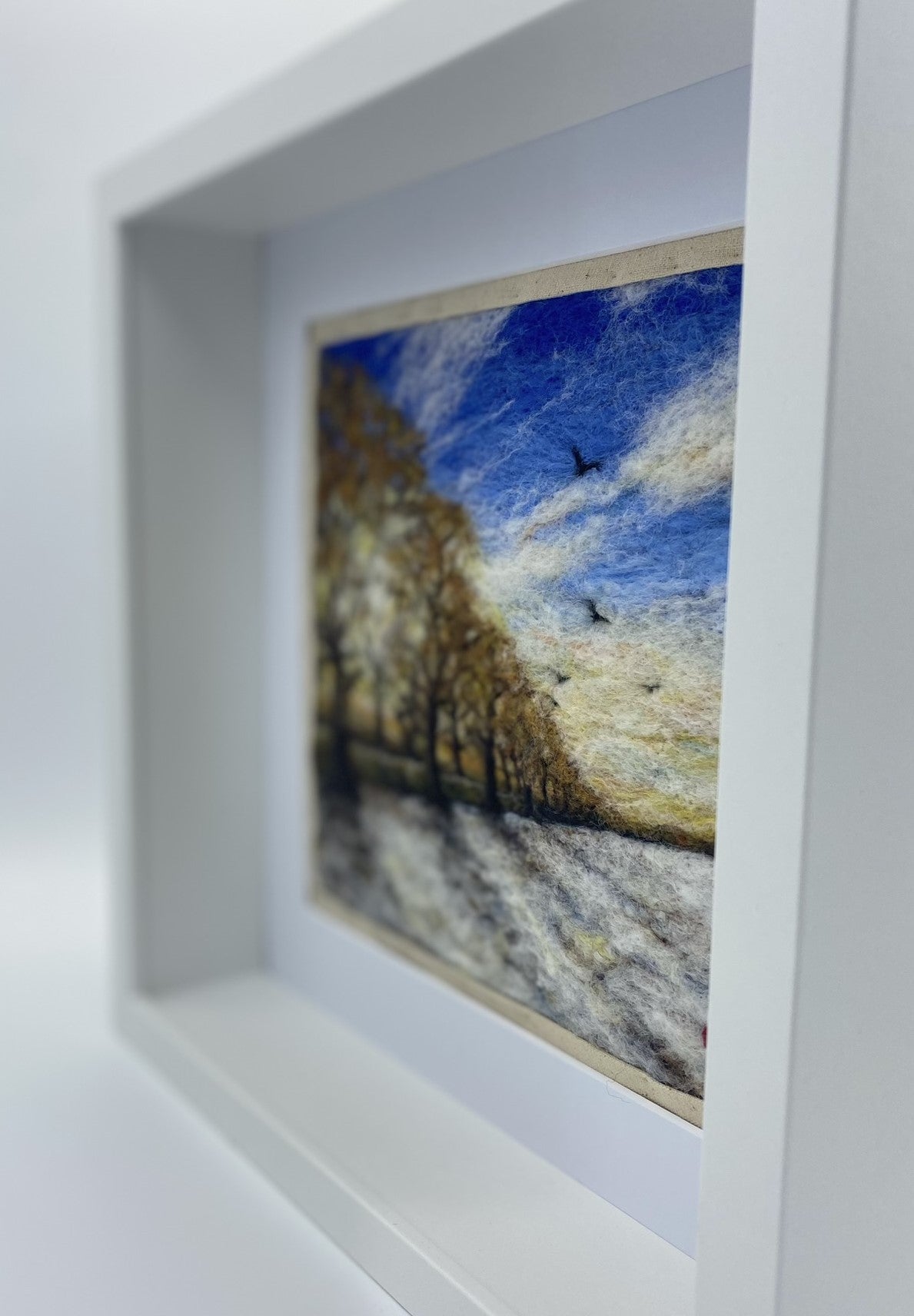 needle felted scene of a wintery sunrise with a row of almost bare trees following a lane to a distant horizon; the trees are casting shadows on a snowy field