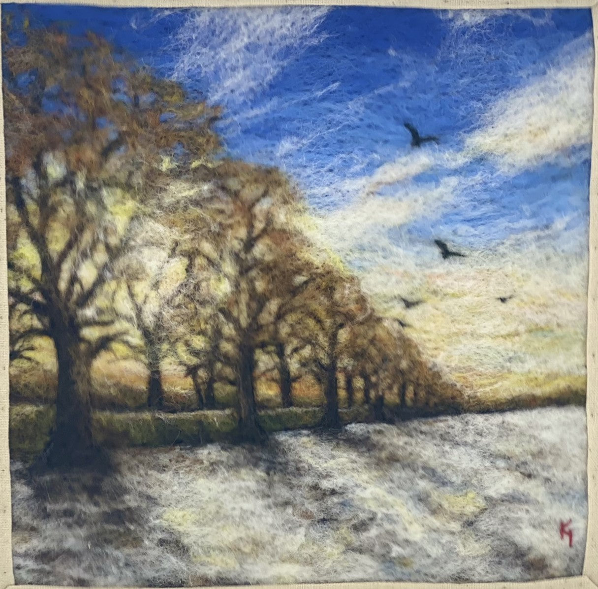 needle felted scene of a wintery sunrise with a row of almost bare trees following a lane to a distant horizon; the trees are casting shadows on a snowy field