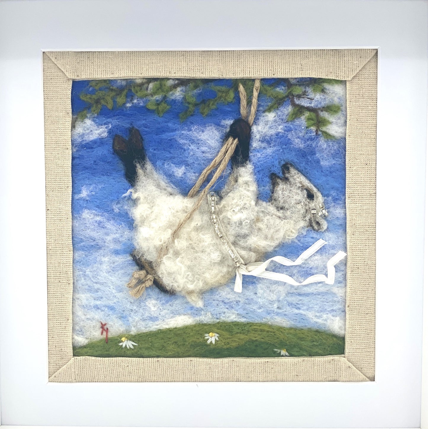 needle felted picture of a sheep on a swing wearing a beaded ribbon belt