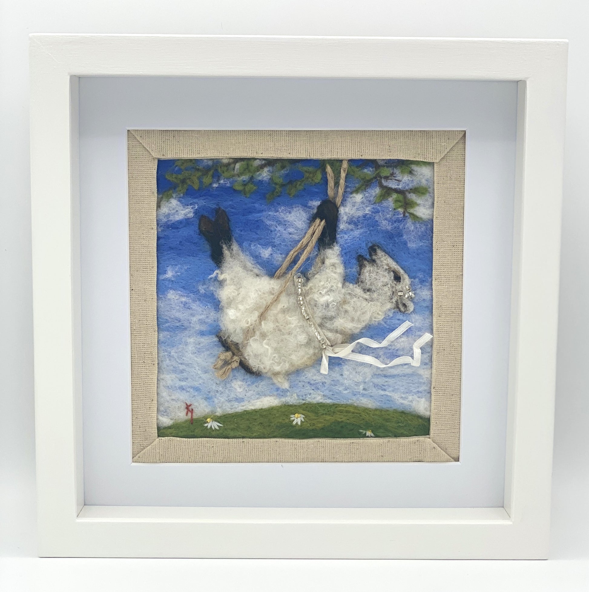 needle felted picture of a sheep on a swing wearing a beaded ribbon belt