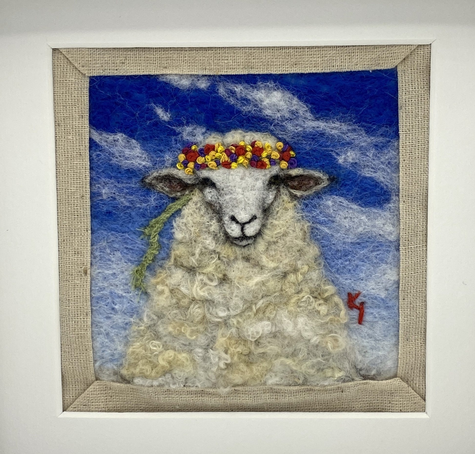 needle felted portrait of a sheep wearing a mulitcoloured stitched crown on a sky blue floral background