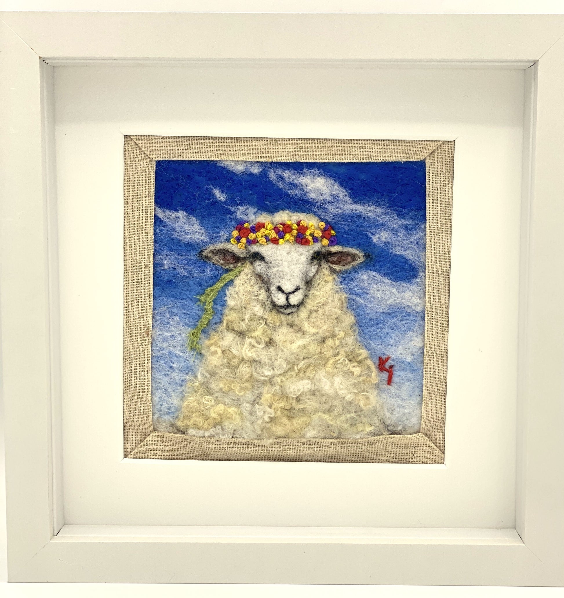 needle felted portrait of a sheep wearing a mulitcoloured stitched crown on a sky blue floral background