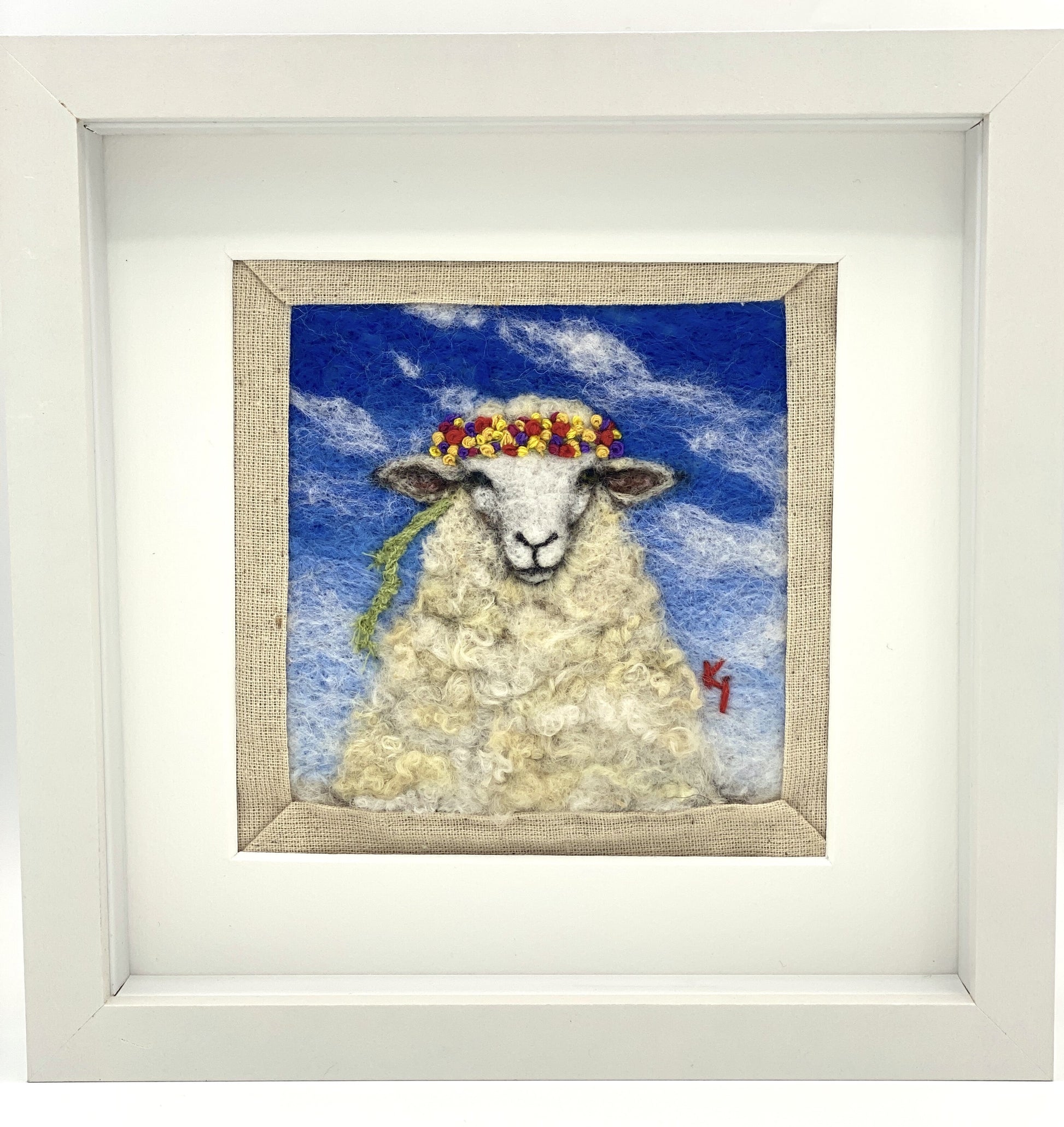 needle felted portrait of a sheep wearing a mulitcoloured stitched crown on a sky blue floral background