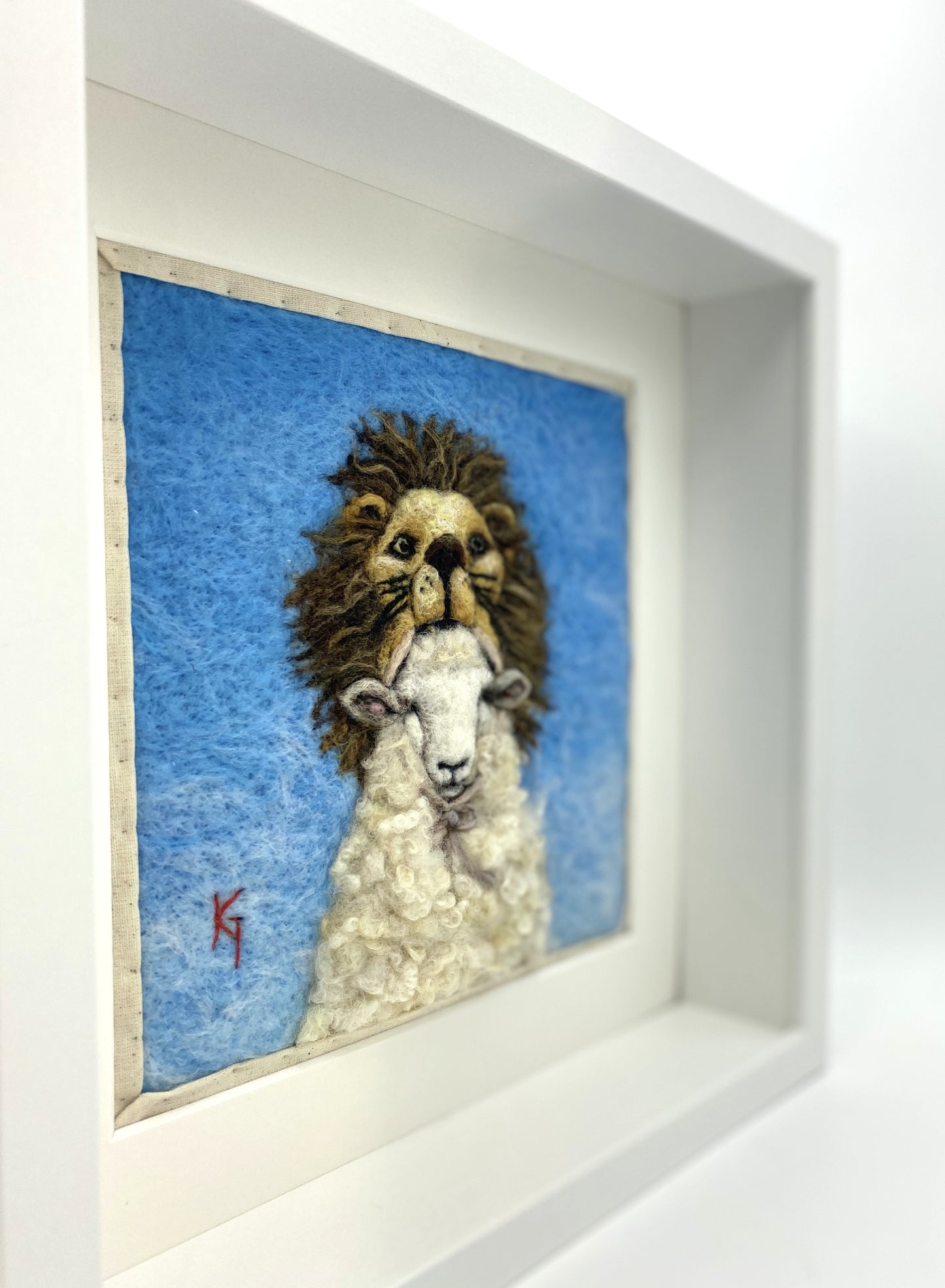 Needle felted framed depiction of a sheep with a lion headdress, with a blue background