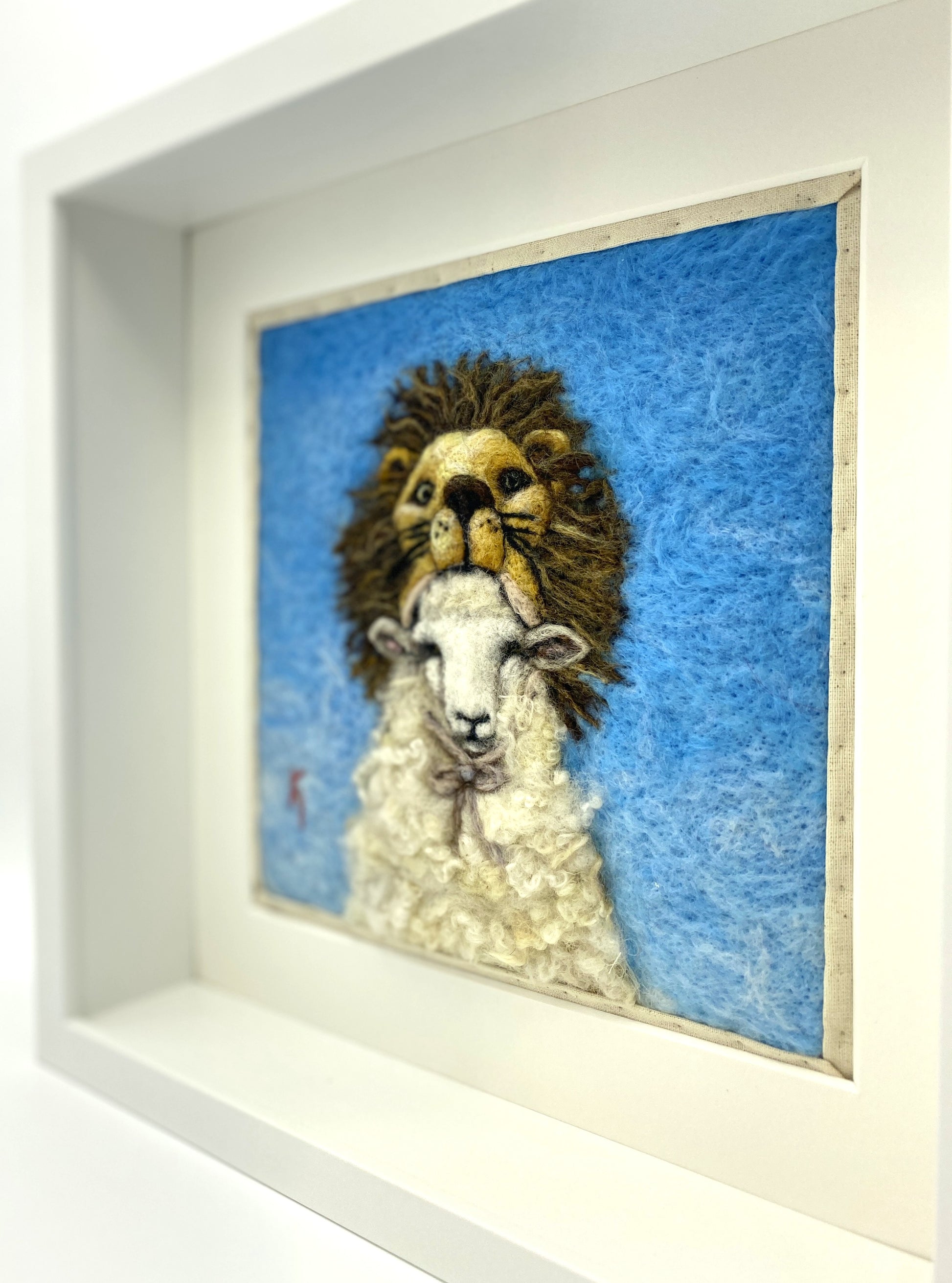 Needle felted framed depiction of a sheep with a lion headdress, with a blue background
