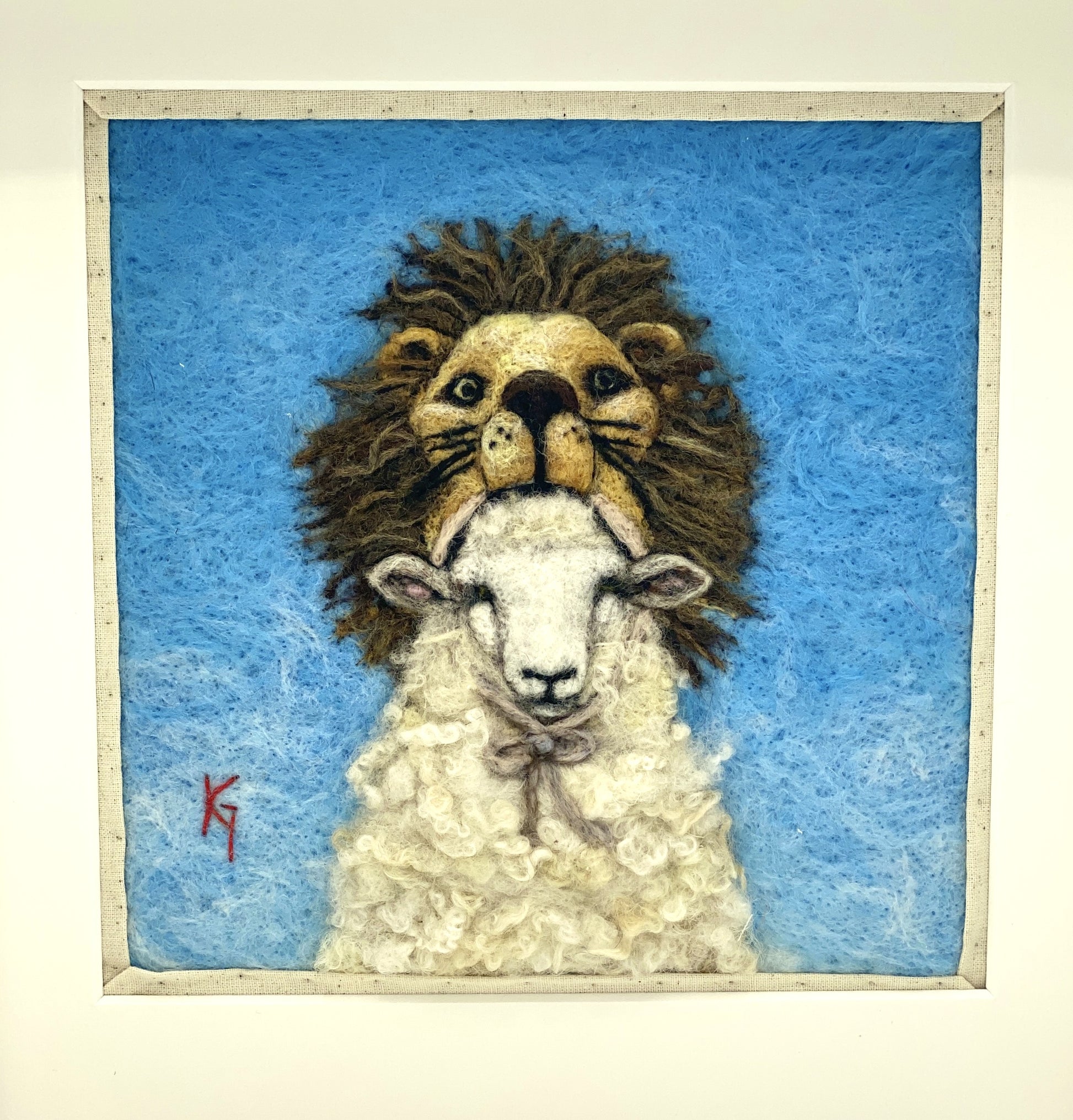 Needle felted framed depiction of a sheep with a lion headdress, with a blue background