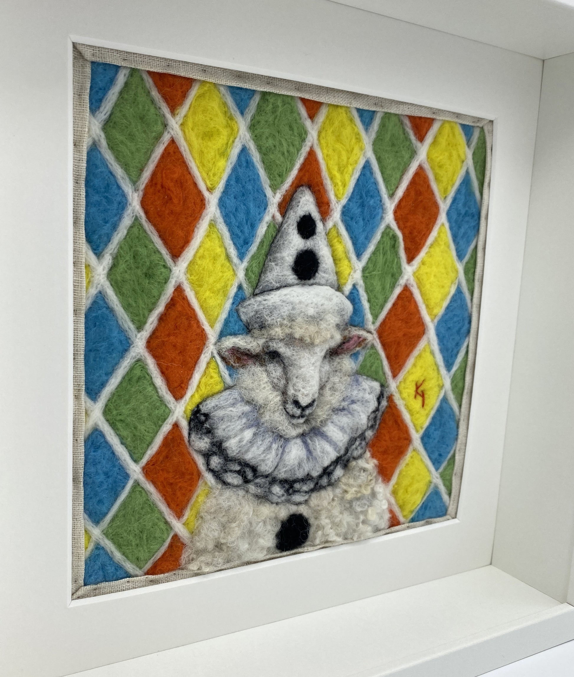 needle felted sheep dressed in Pierrot costume with harlequin background