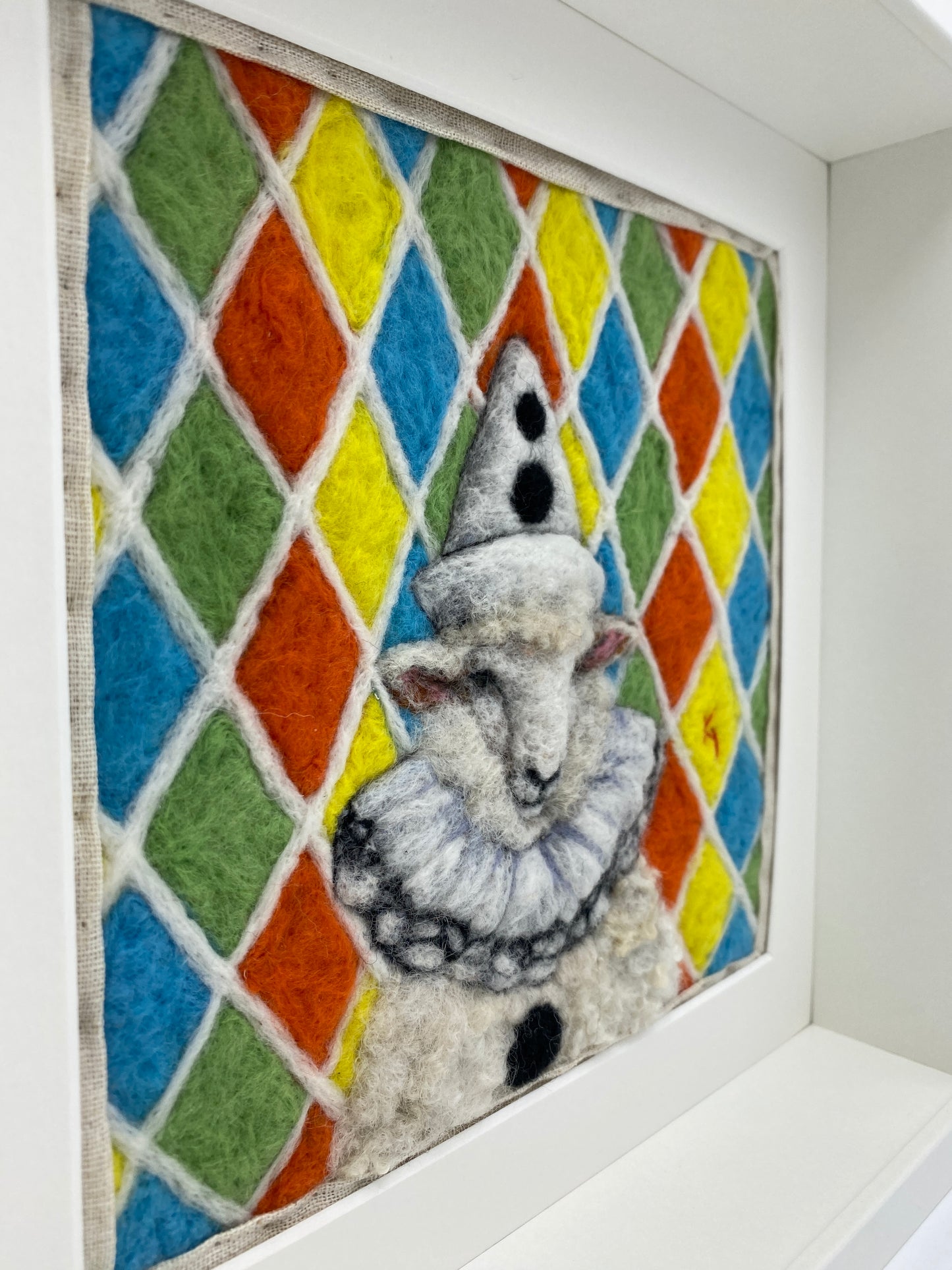 needle felted sheep dressed in Pierrot costume with harlequin background
