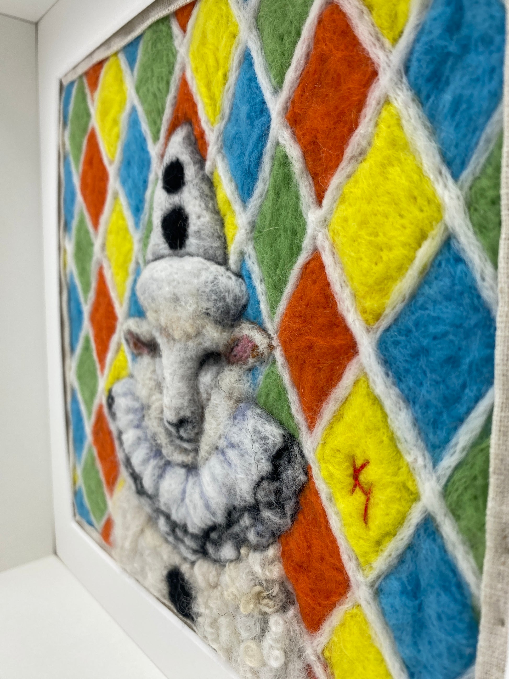 needle felted sheep dressed in Pierrot costume with harlequin background