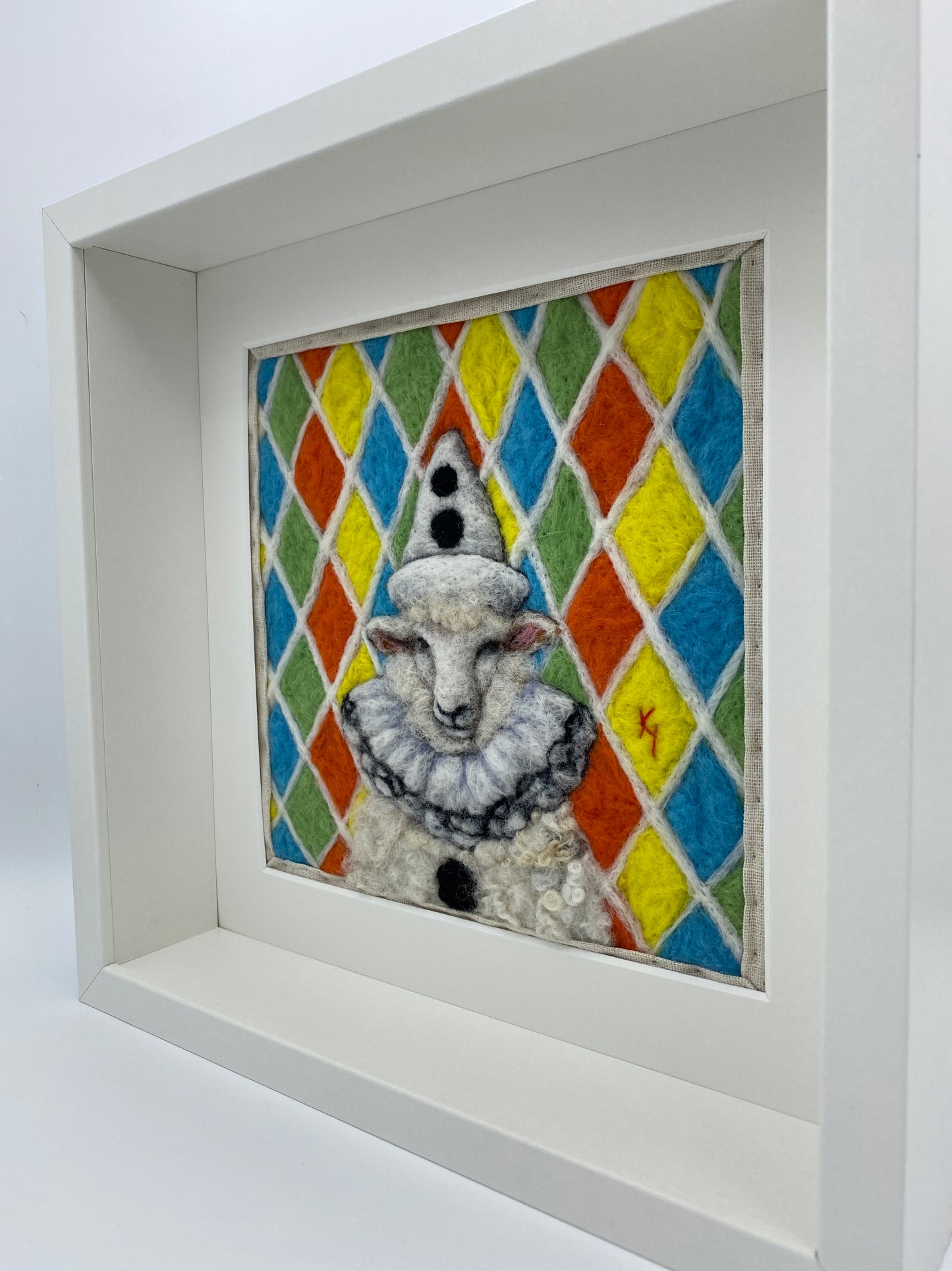needle felted sheep dressed in Pierrot costume with harlequin background