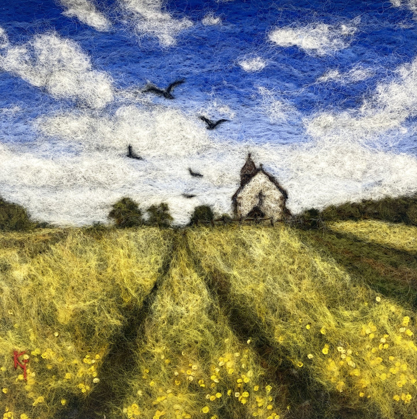 needle felted depiction of a church in a field with birds flying overhead in th cloudy blue sky