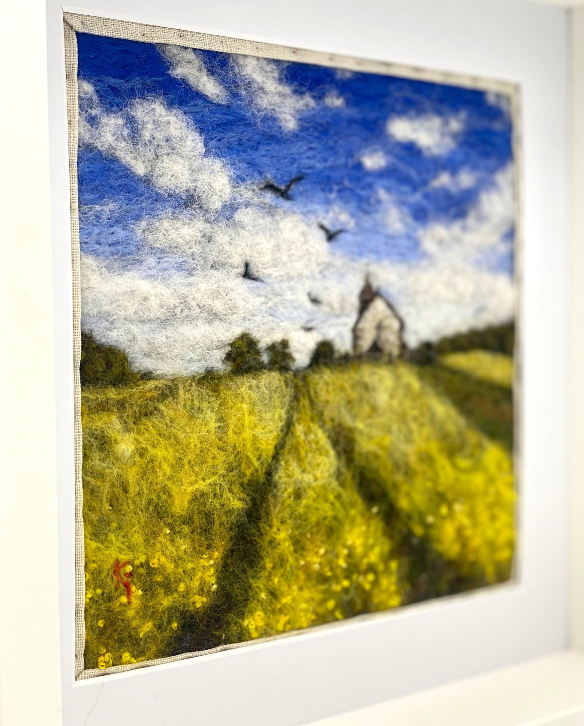 Framed artwork of a landscape with yellow field, blue sky, and birds.