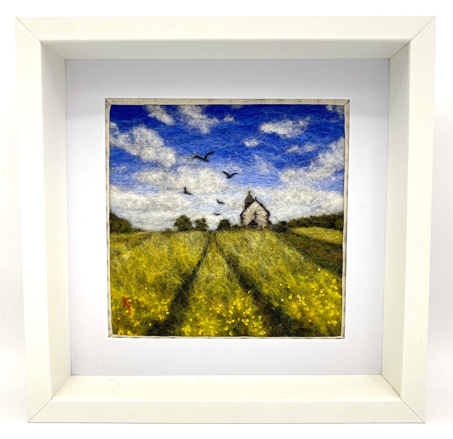 needle felted depiction of a church in a field with birds flying overhead in th cloudy blue sky