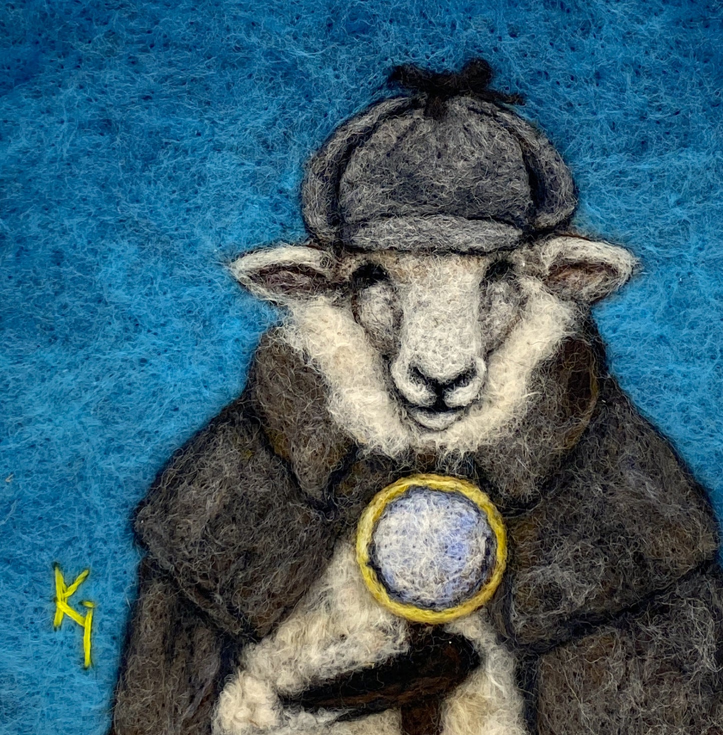 needle felted framed art work of a sheep dressed as Shelock Holmes in coat, deer stalker hat and holding a magnifying glass