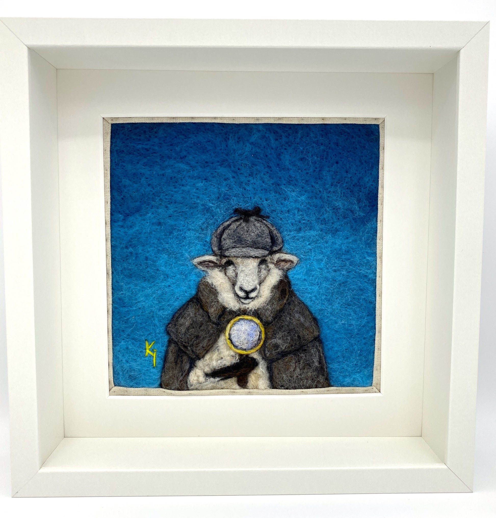 needle felted framed art work of a sheep dressed as Shelock Holmes in coat, deer stalker hat and holding a magnifying glass