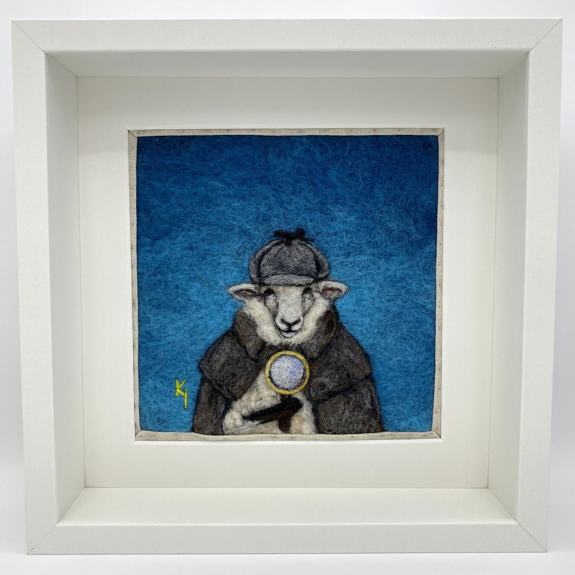 needle felted framed art work of a sheep dressed as Shelock Holmes in coat, deer stalker hat and holding a magnifying glass