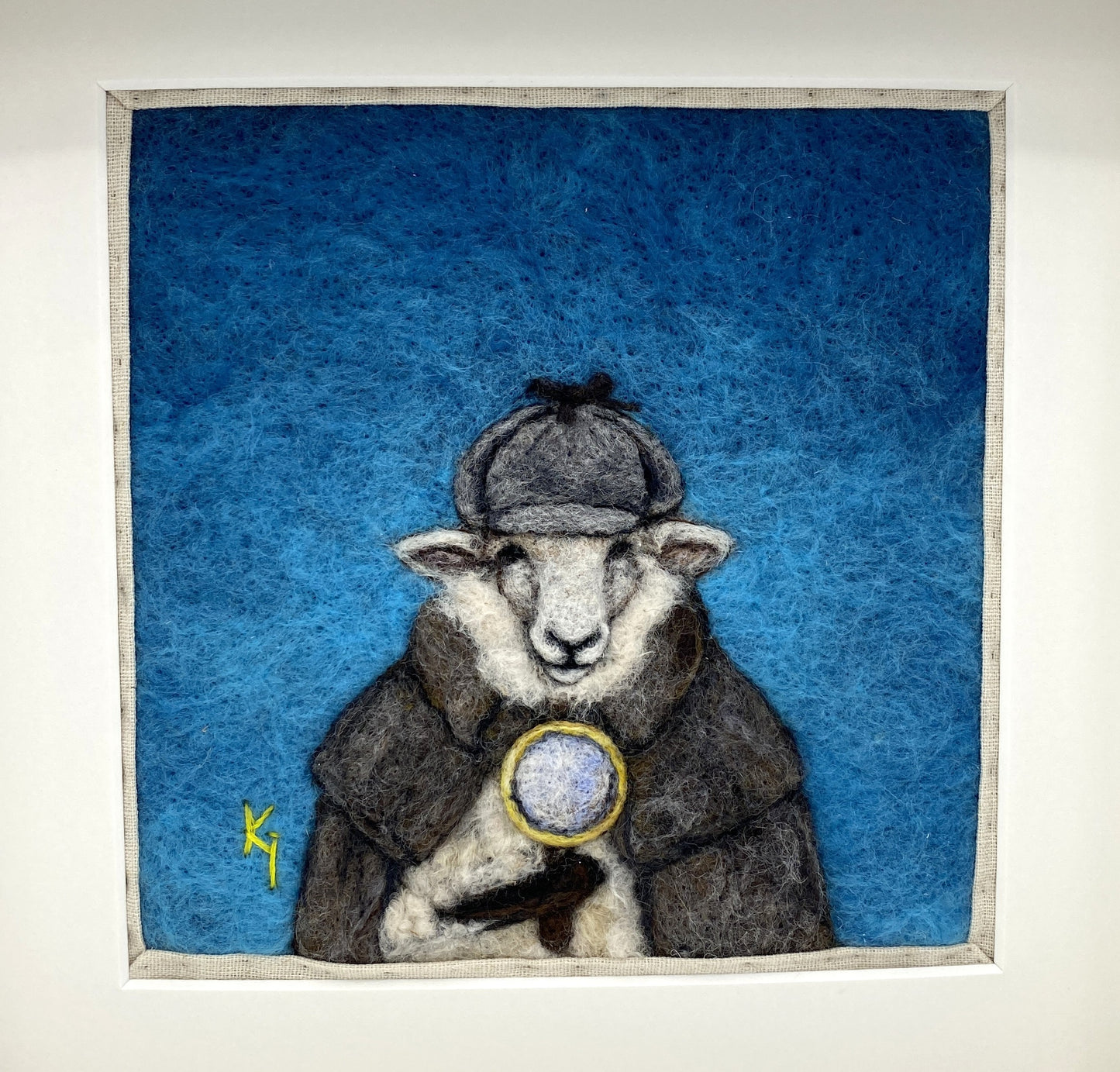 needle felted framed art work of a sheep dressed as Shelock Holmes in coat, deer stalker hat and holding a magnifying glass
