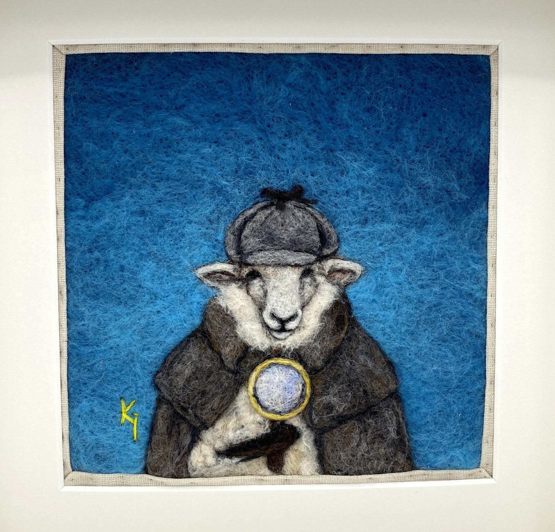 needle felted framed art work of a sheep dressed as Shelock Holmes in coat, deer stalker hat and holding a magnifying glass