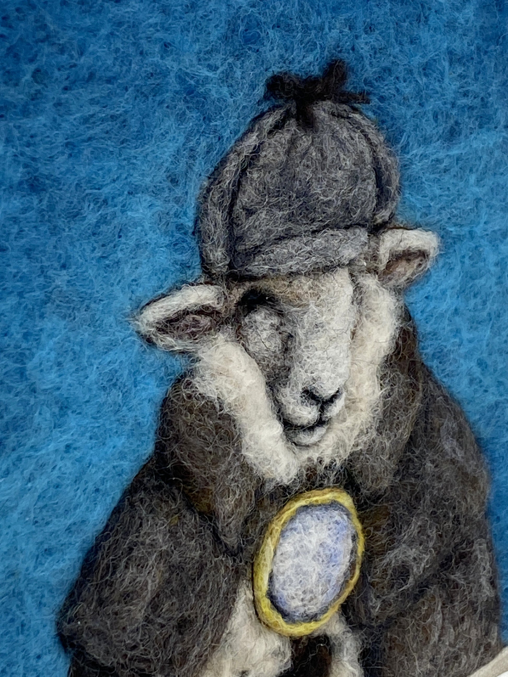 needle felted framed art work of a sheep dressed as Shelock Holmes in coat, deer stalker hat and holding a magnifying glass