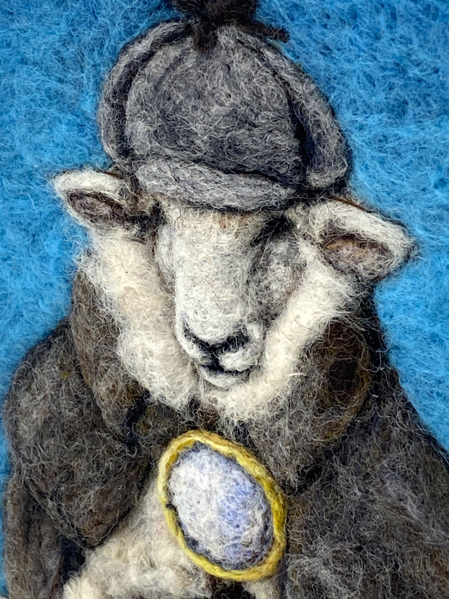 needle felted framed art work of a sheep dressed as Shelock Holmes in coat, deer stalker hat and holding a magnifying glass