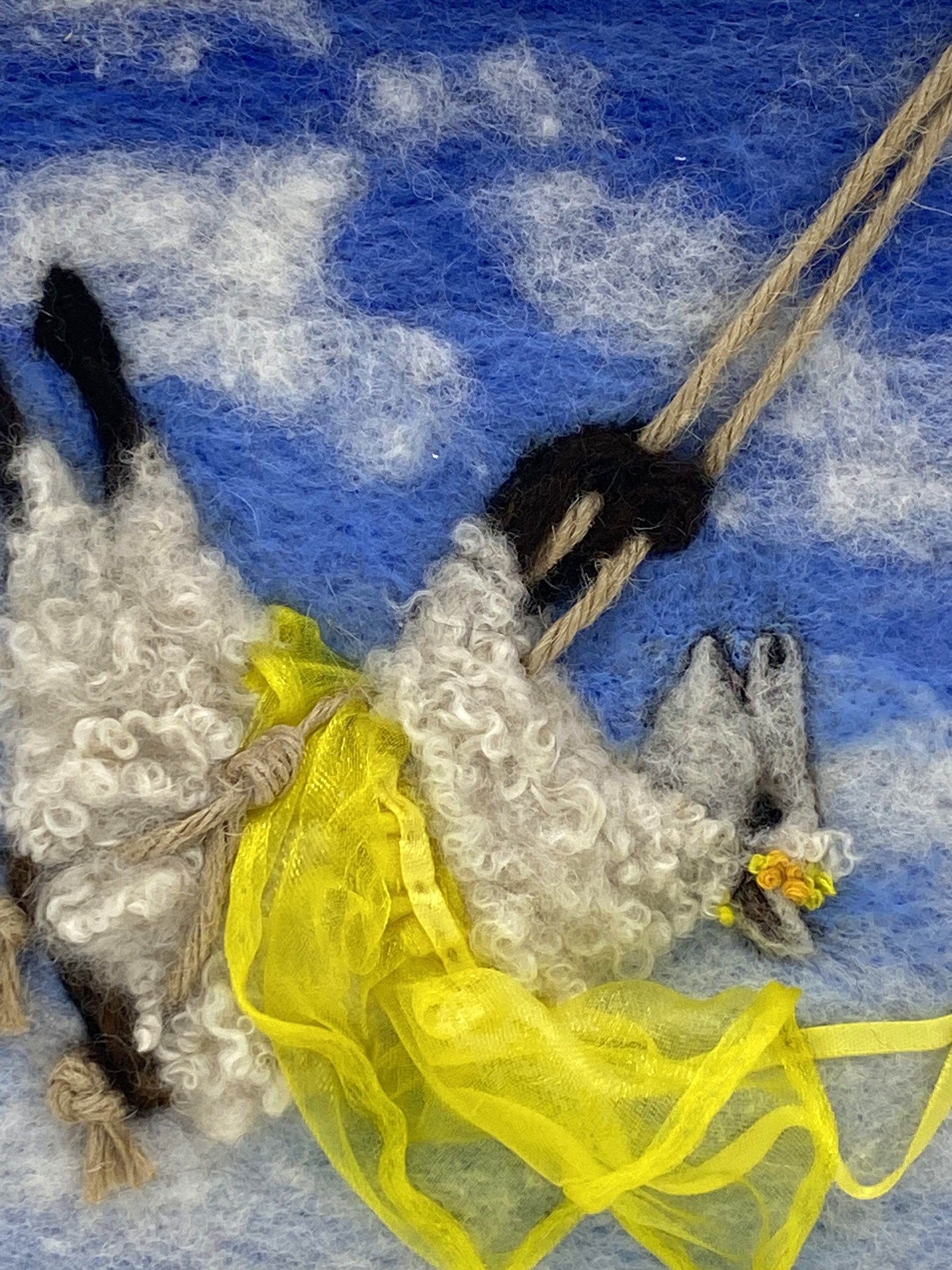 needle felted art work depicting a sheep on a swing wearing a yellow skirt