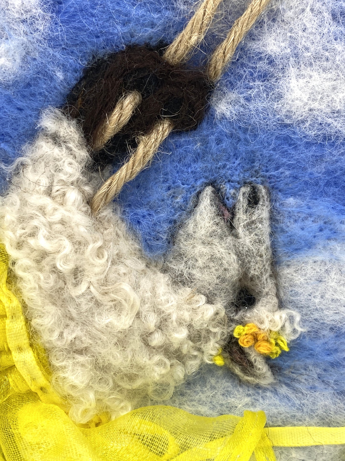 needle felted art work depicting a sheep on a swing wearing a yellow skirt