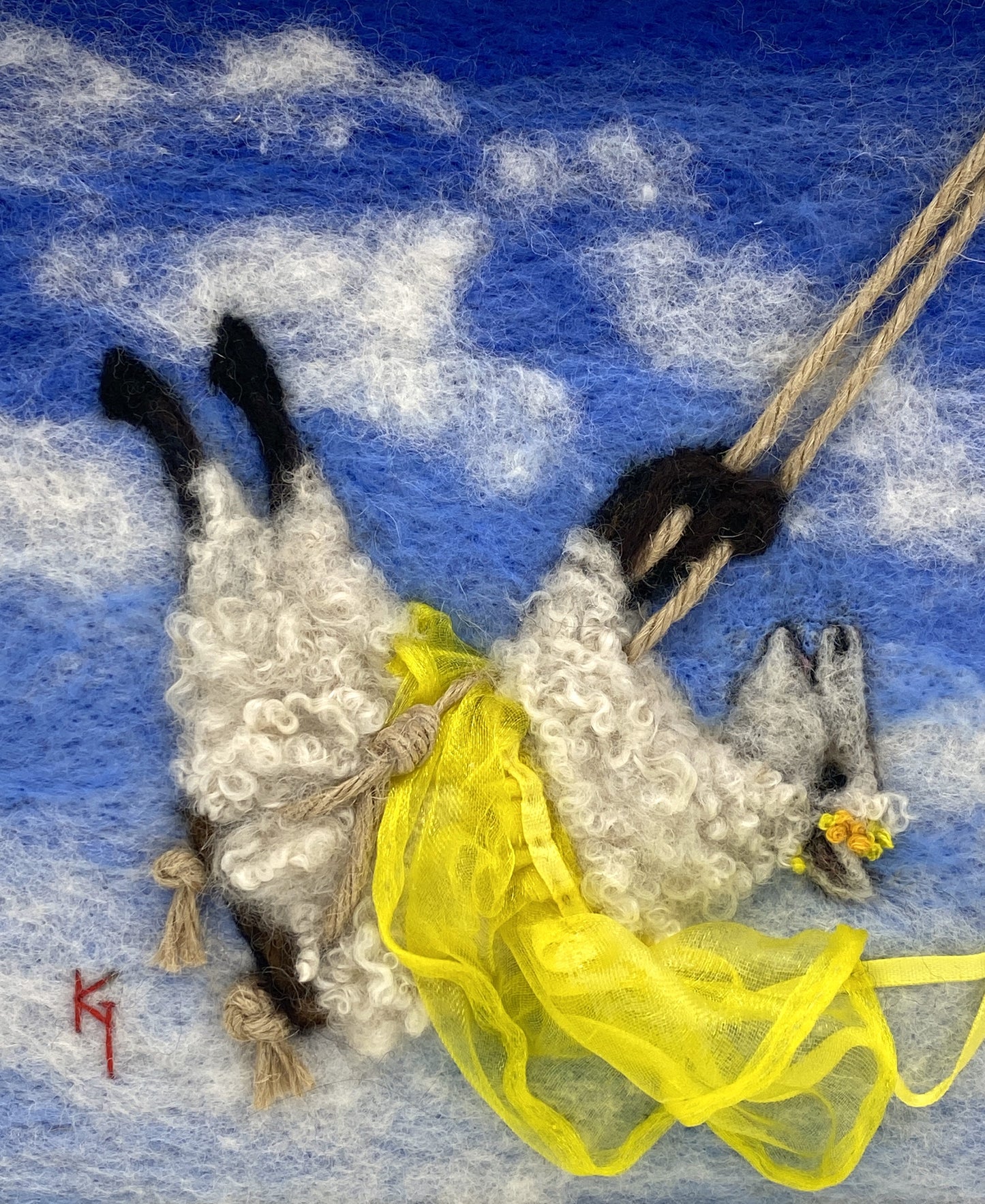 needle felted art work depicting a sheep on a swing wearing a yellow skirt