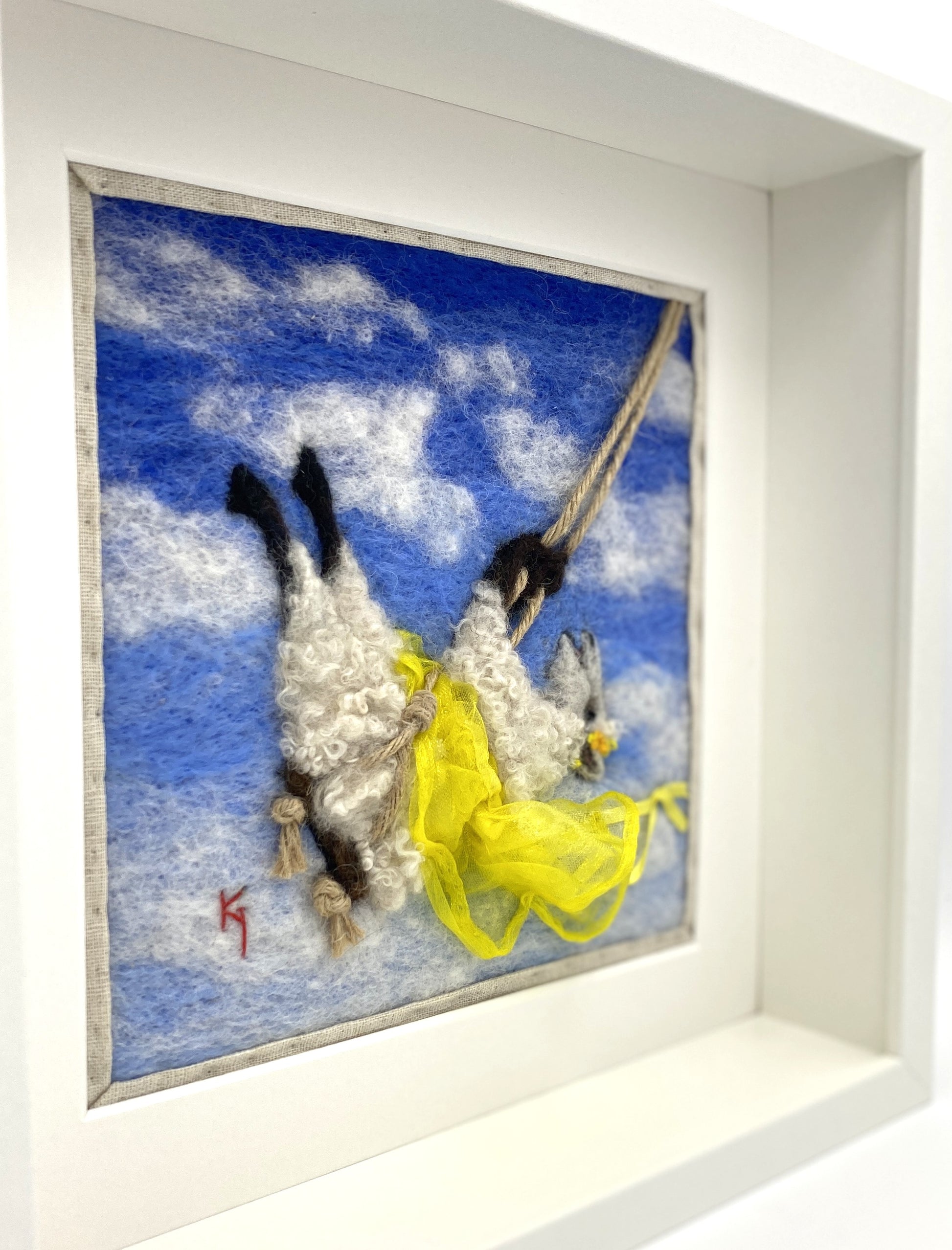 needle felted art work depicting a sheep on a swing wearing a yellow skirt