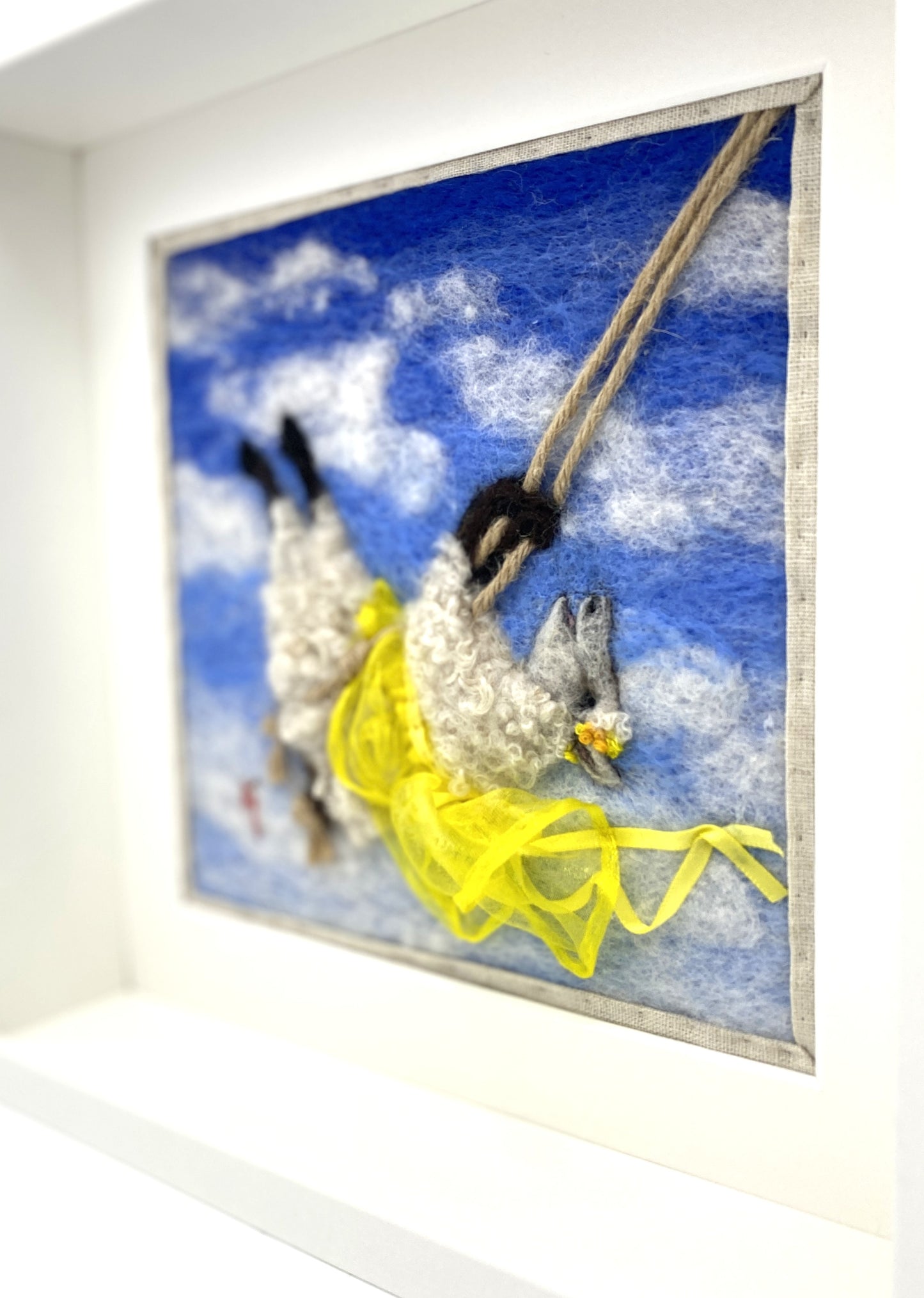 needle felted art work depicting a sheep on a swing wearing a yellow skirt