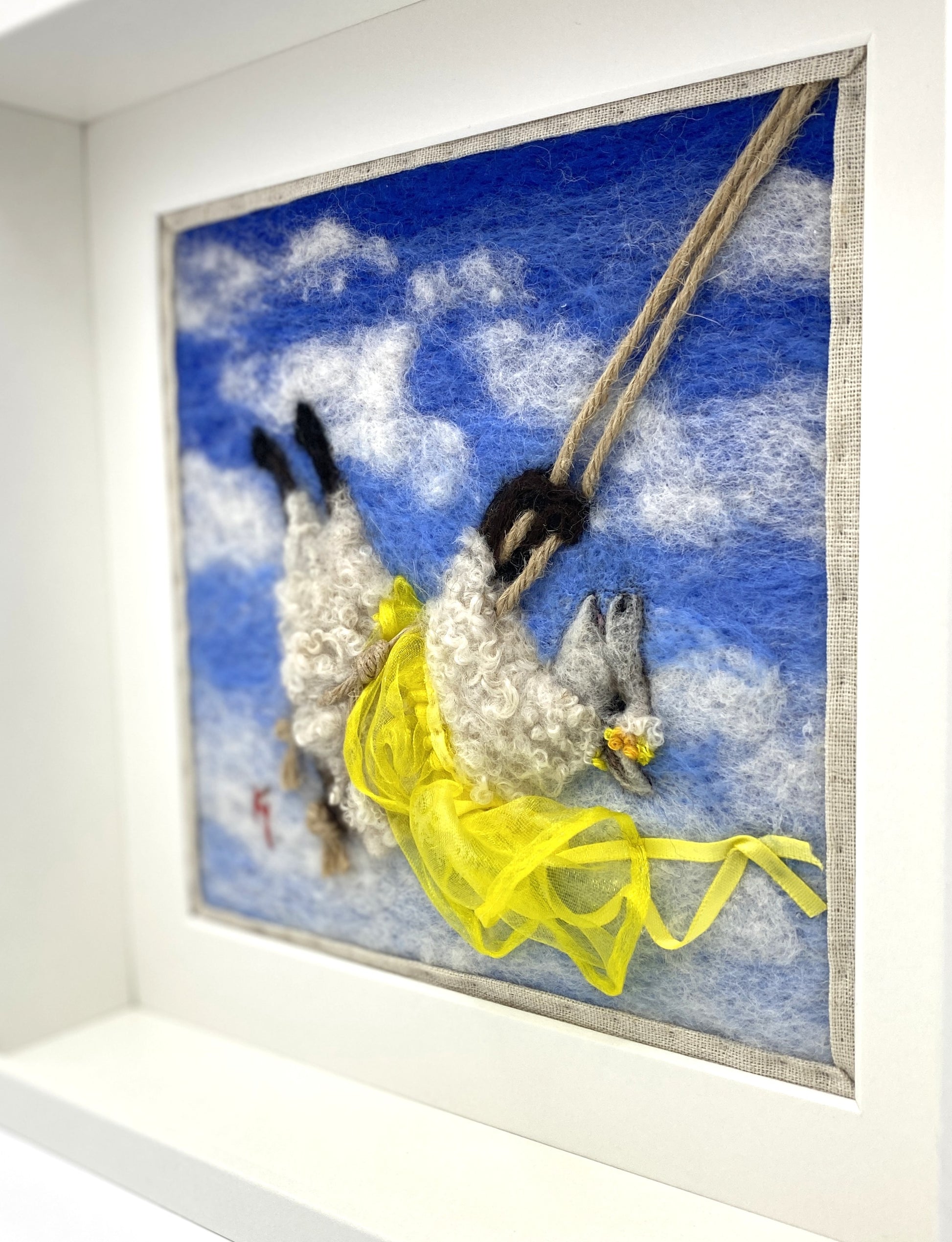 needle felted art work depicting a sheep on a swing wearing a yellow skirt