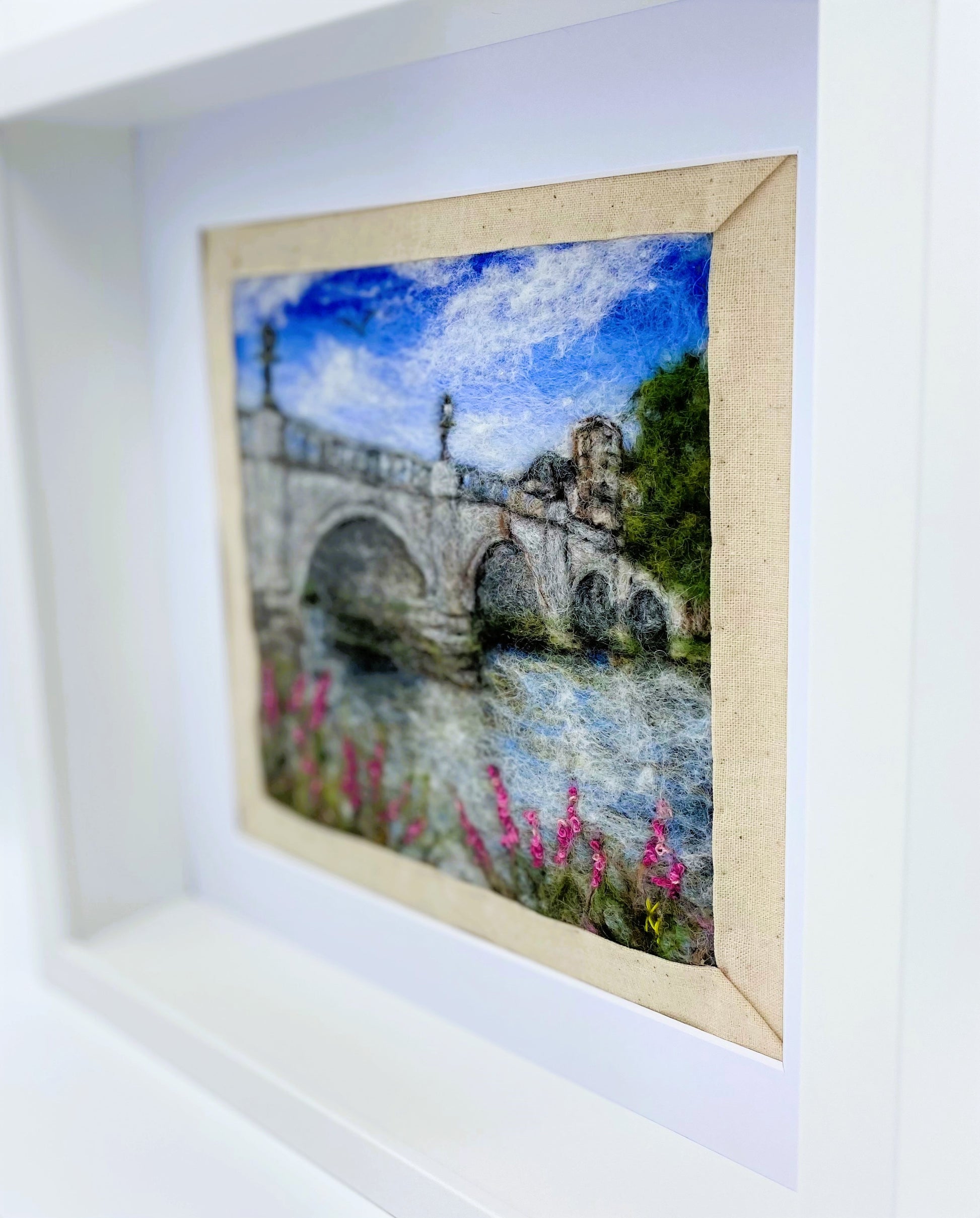 a box-framed, needle felted wool fibre picture of Ricmond Bridge showing the bridge, buildings across the river, trees, lamp posts and embroidered purple wild flowers