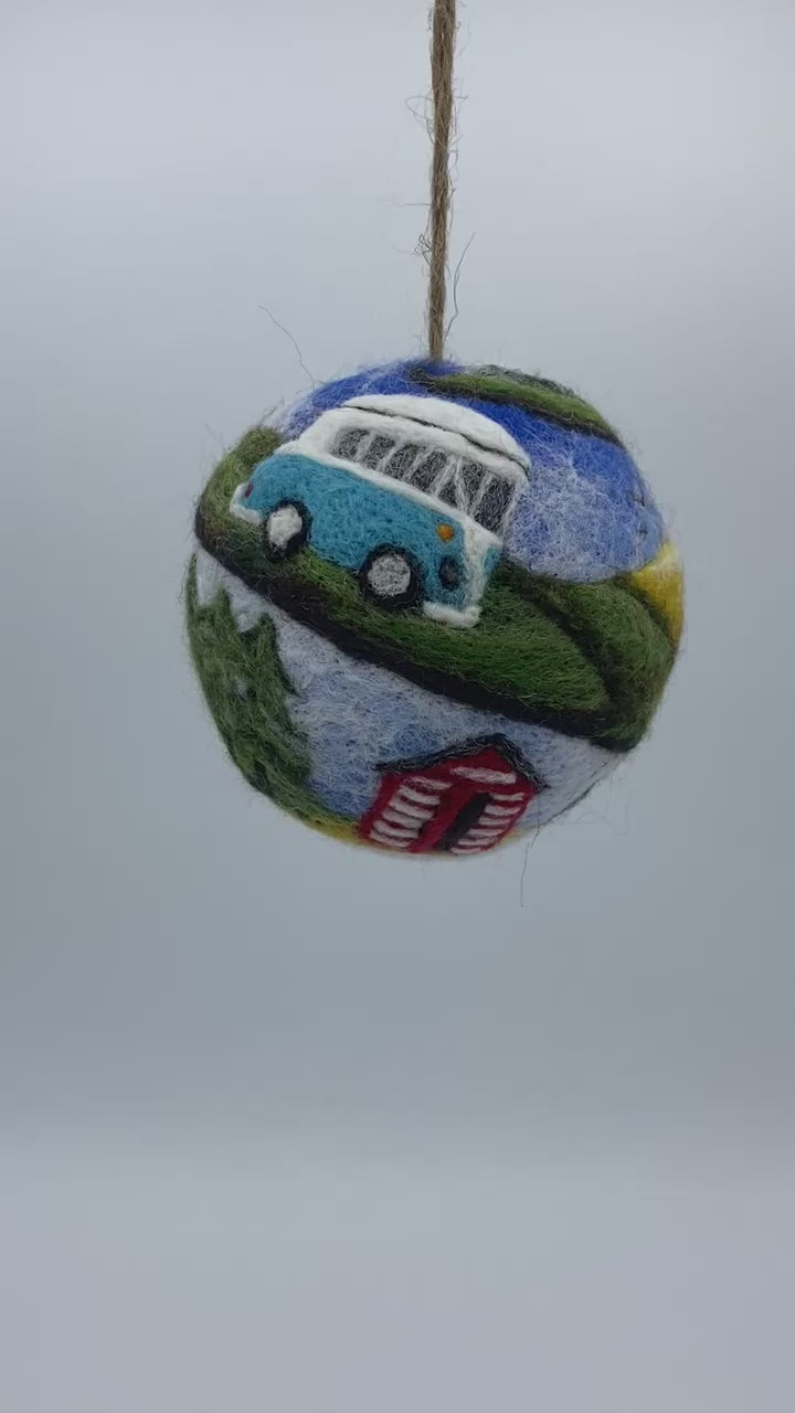 needle felted bauble depicting a camper van travelling through mountains, camping site and countryside and finally reaching the beach hut by the sea