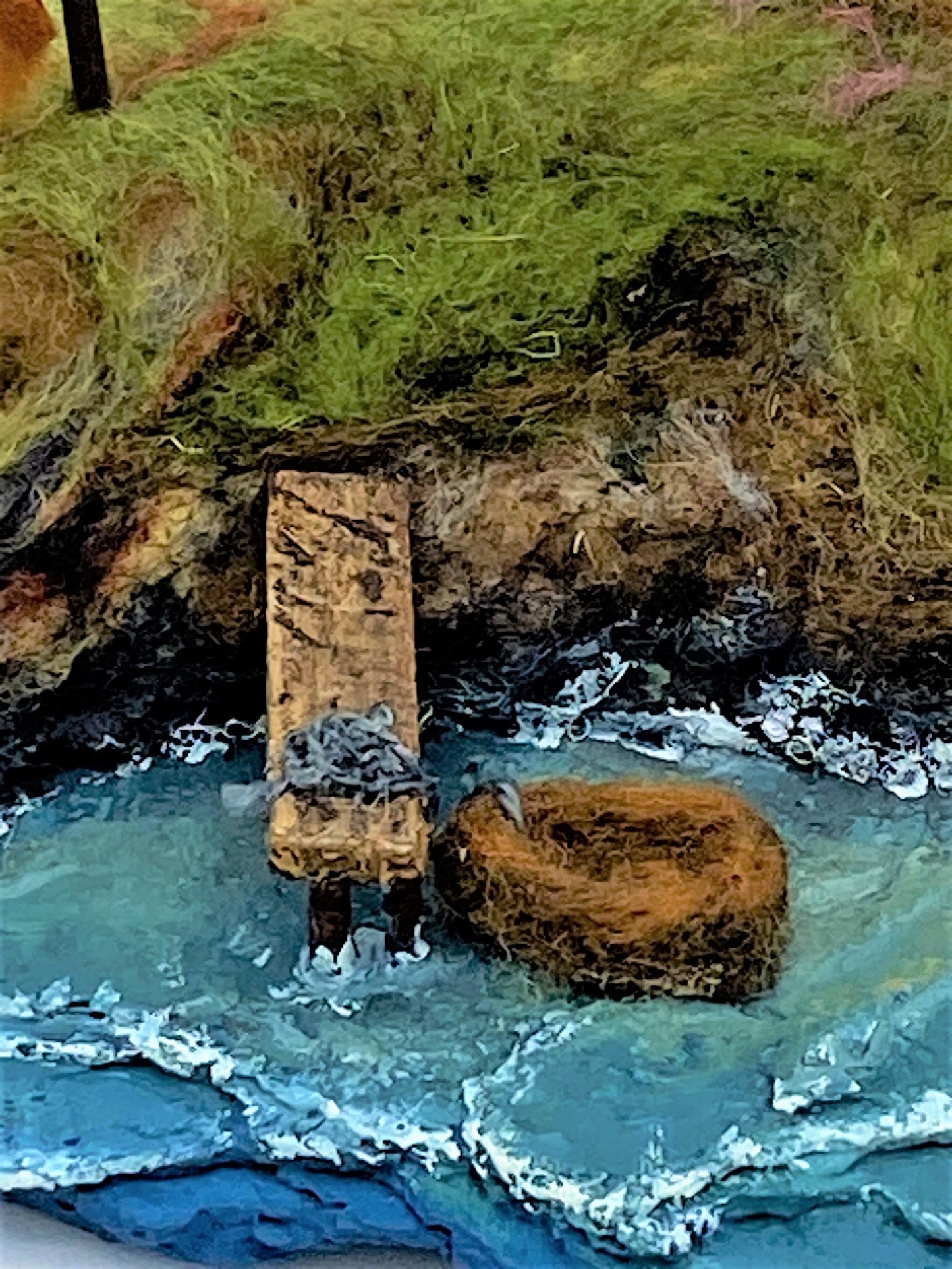 close up of needle felted red and white striped lighthouse on rocky island, sea, beach, white house, washing line, wooden dock and woollen boat