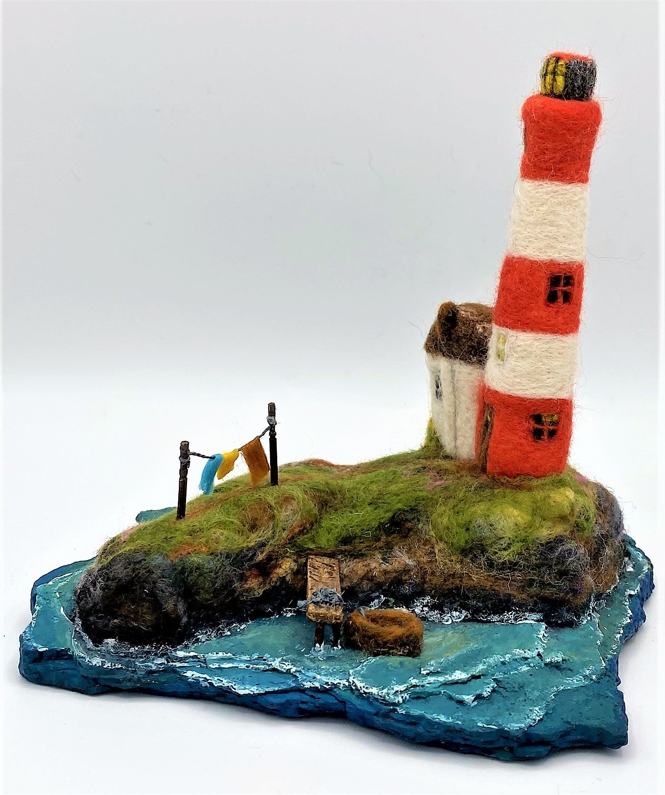 needle felted red and white striped lighthouse on rocky island, sea, beach, white house, washing line, wooden dock and woollen boat