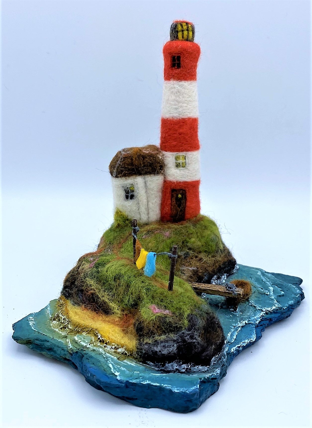 needle felted red and white striped lighthouse on rocky island, sea, beach, white house, washing line, wooden dock and woollen boat