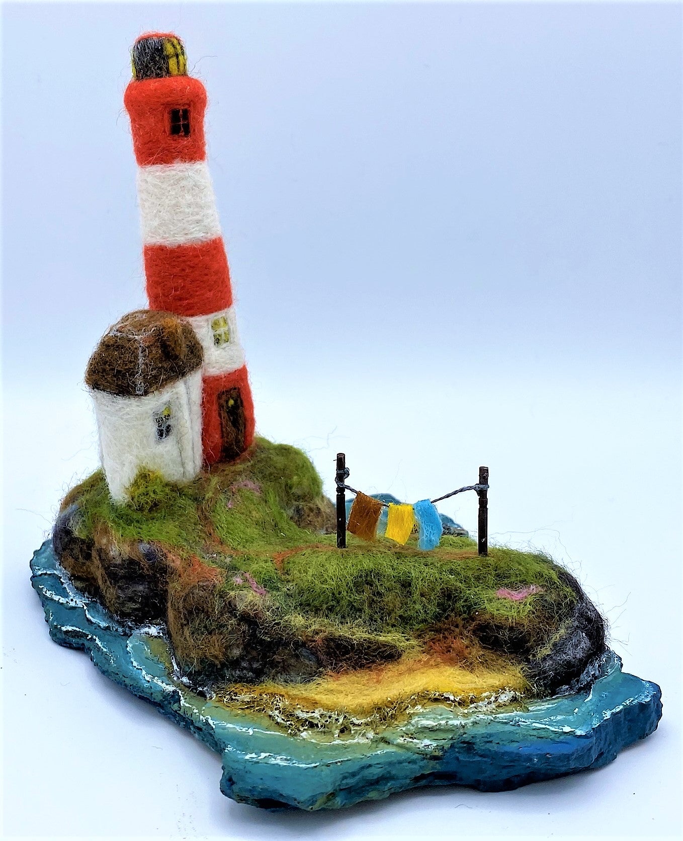 needle felted red and white striped lighthouse on rocky island, sea, beach, white house, washing line, wooden dock and woollen boat