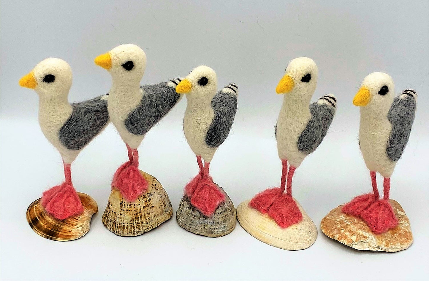 group of five needle felted seagulls standing on sea shells, white, black, grey wings, pink legs and feet